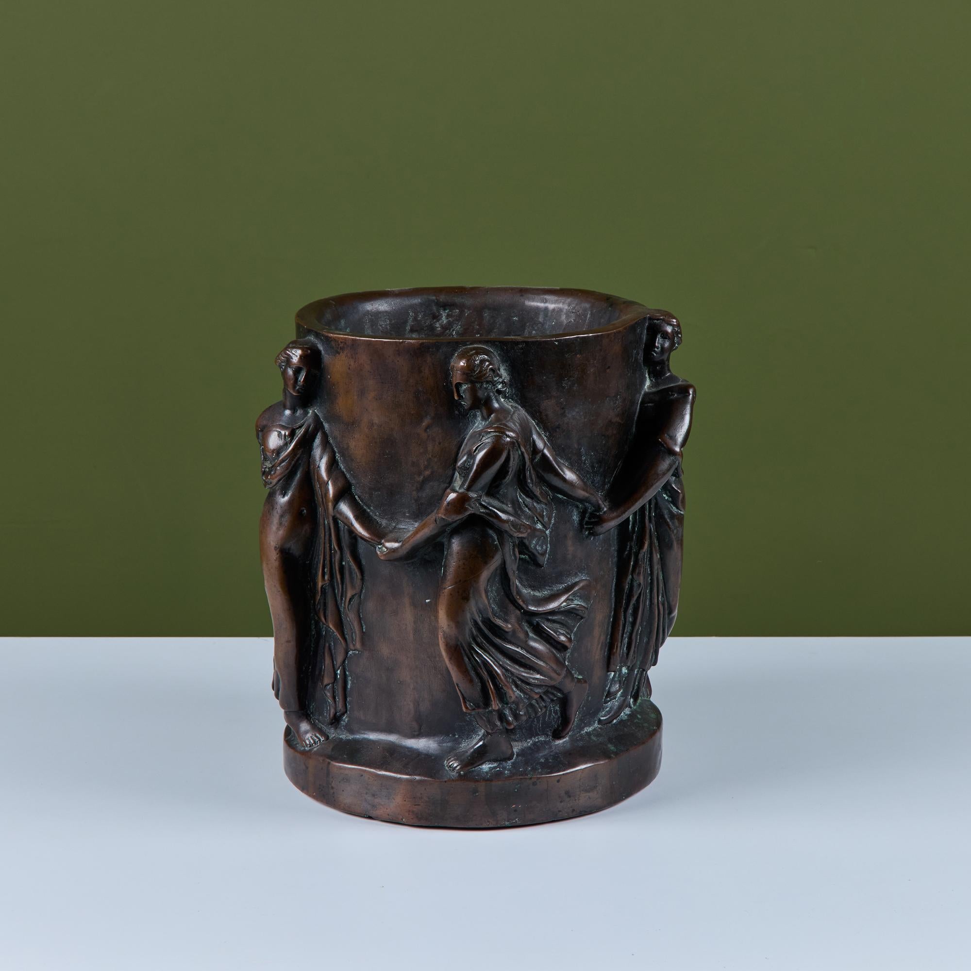 Plaster planter with a bronze colored coating. The planter depicts figures draped in cloth holding hands around the planter.

Dimensions
11.5