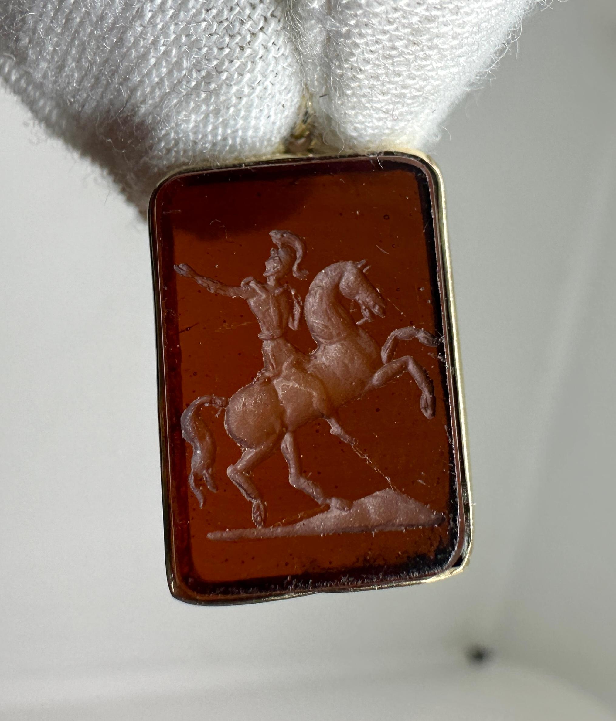 Offrez-vous un pendentif ou une breloque en intaille en pierre dure cornaline sculptée à la main et de style victorien, avec l'image d'un guerrier romain sur son cheval en train de se cabrer, le tout serti dans de l'or 14 carats.
Le pendentif en