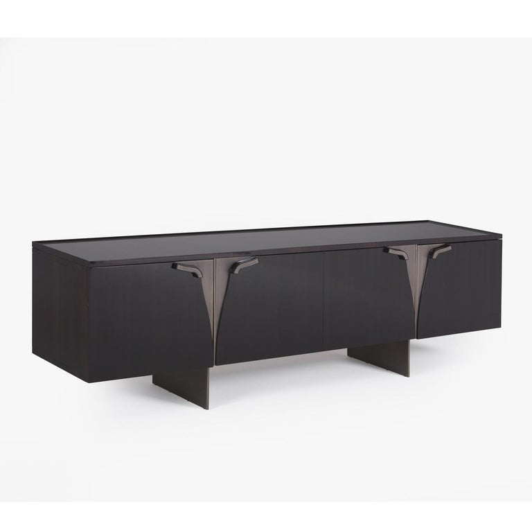 This sideboard boasts an innovative and unique design with a sturdy block supported by two thin, vertical panels. This piece is entirely handcrafted of eucalyptus wood boasting a dark, natural hue, and enriched with bronzed brass details.
  