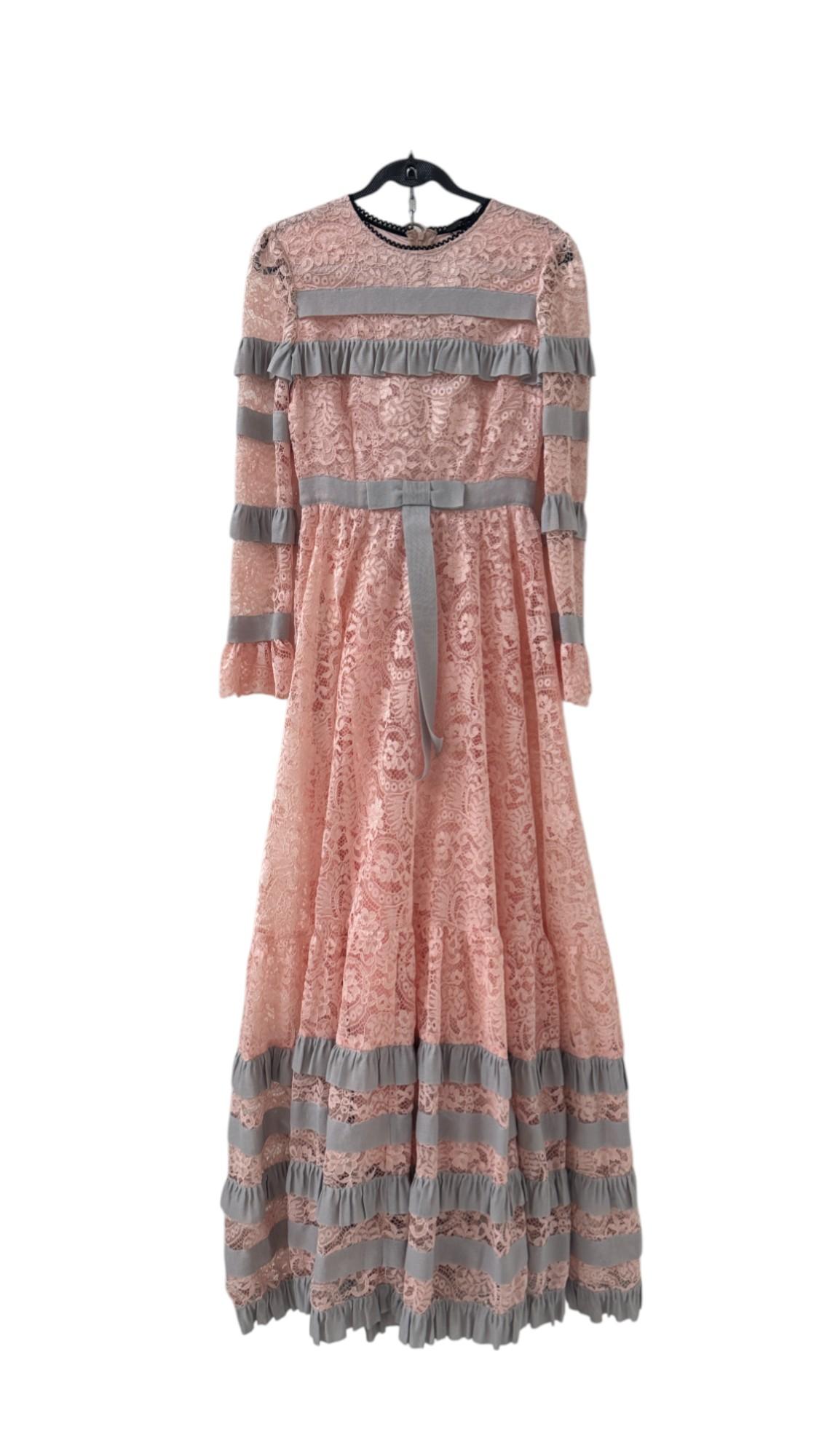 Step into a fairytale with this breathtaking full-length gown by K-QUINN, part of the Altergodress line. Crafted in a soft blush pink lace with intricate floral motifs, the dress evokes a timeless romantic charm. Contrasting gray grosgrain ruffles