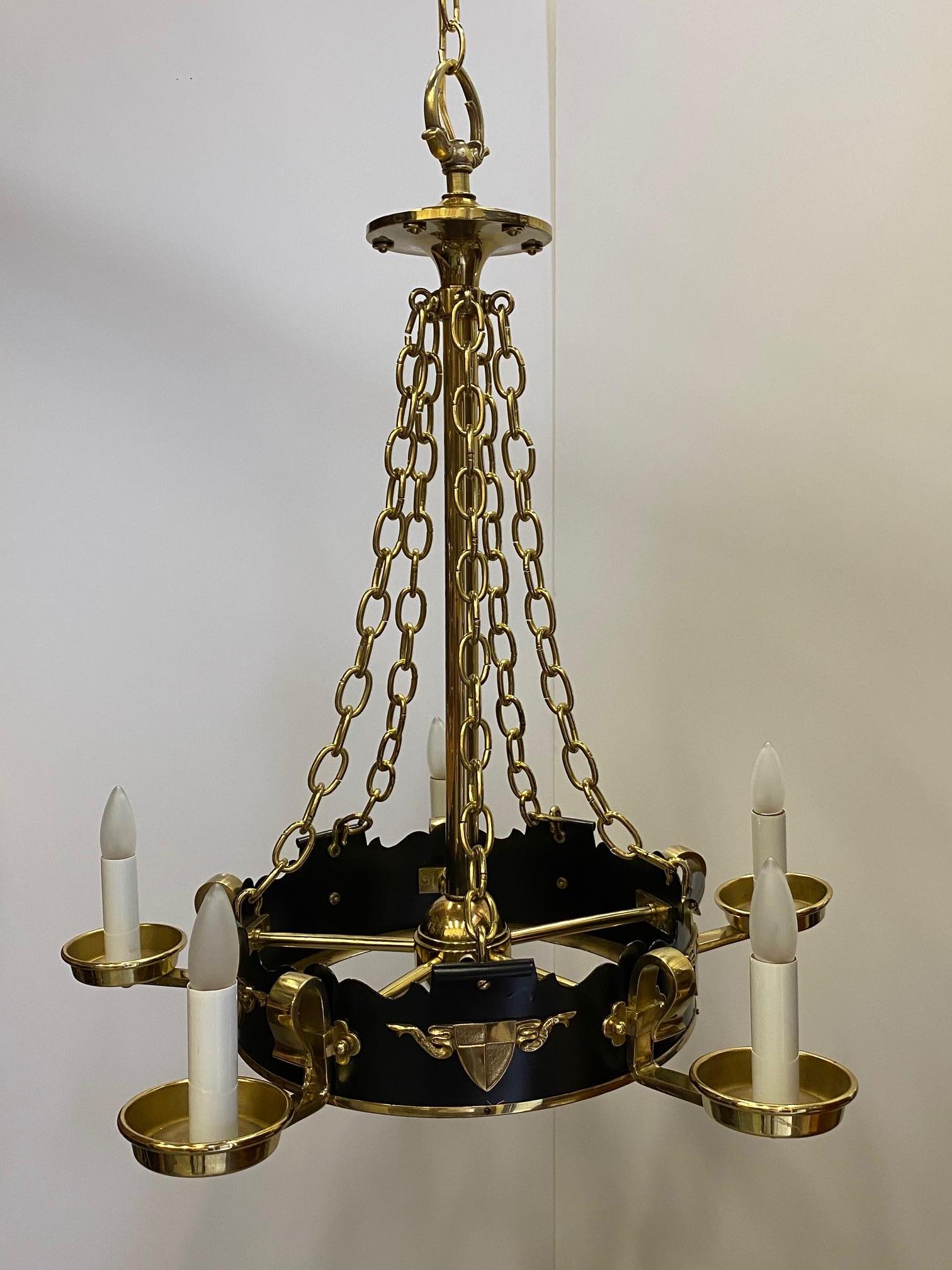 Striking vintage chandelier in black and gold having circular base with 4 extending brass arms with candle lights, suspended from handsome gold chains. Body of fixture has brass crest decoration.