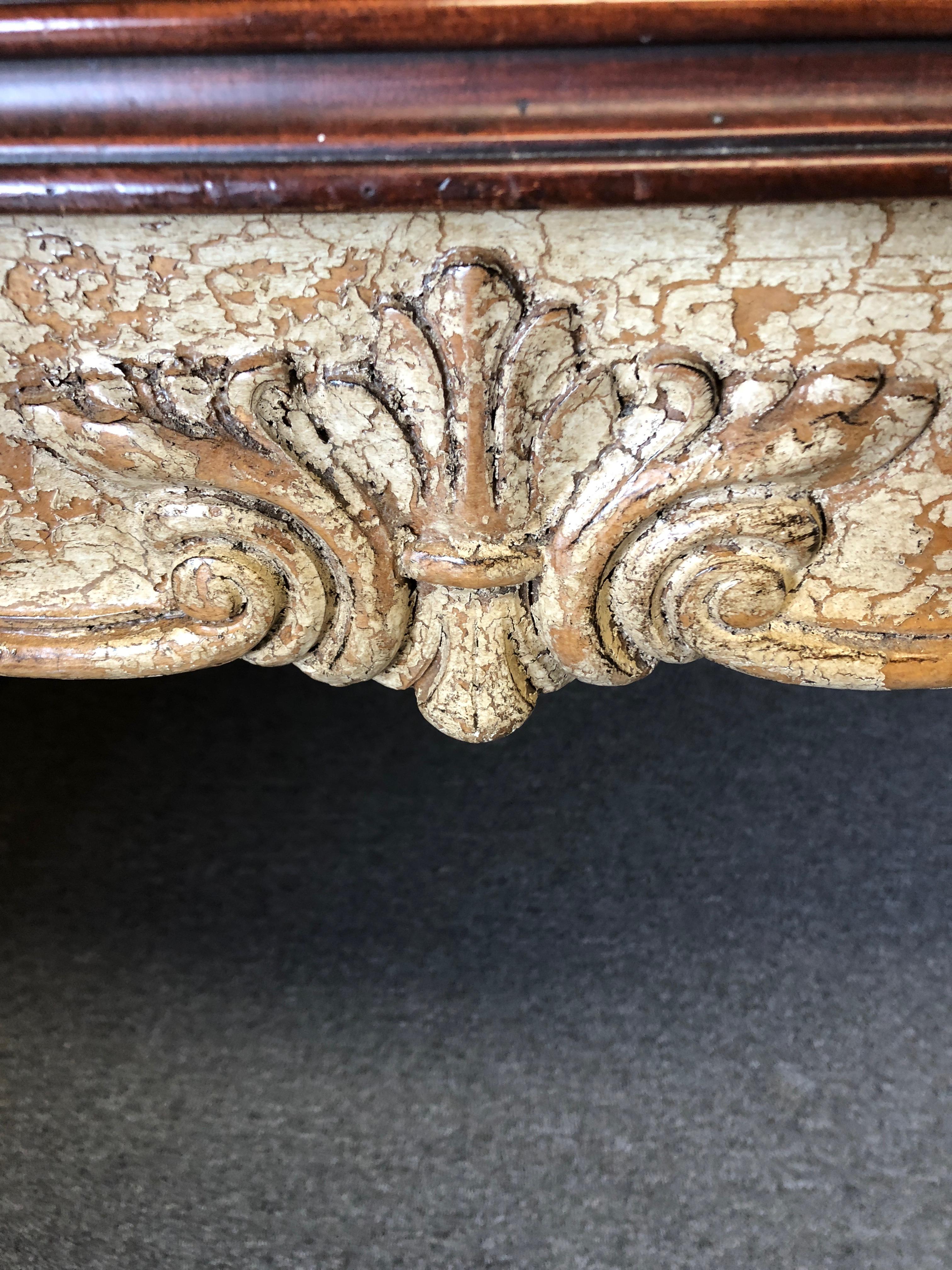 A large romantic French style desk having a warm cherrywood top that contrasts beautifully with the painted distressed ornately carved base with cabriole legs. Decorative carved acanthus leaves, fleur-di-lis, curved feet and single drawer add to its