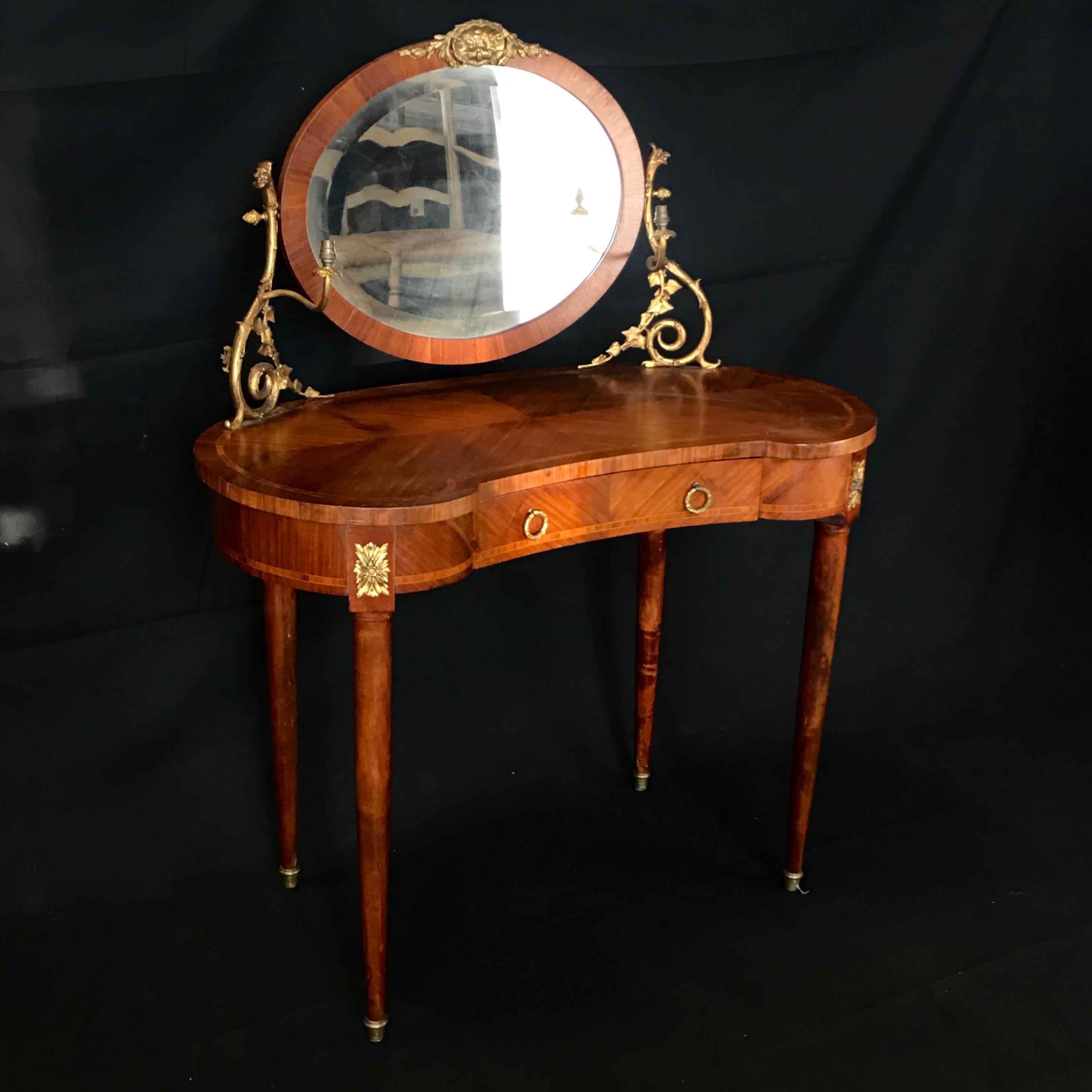 A French inlaid fine dressing table having a kidney shaped top with gilt bronze encadrement and a superstructure supporting an oval mirror flanked by gilt bronze scrolling candle arms, above one center frieze drawer and raised on delicate tapering