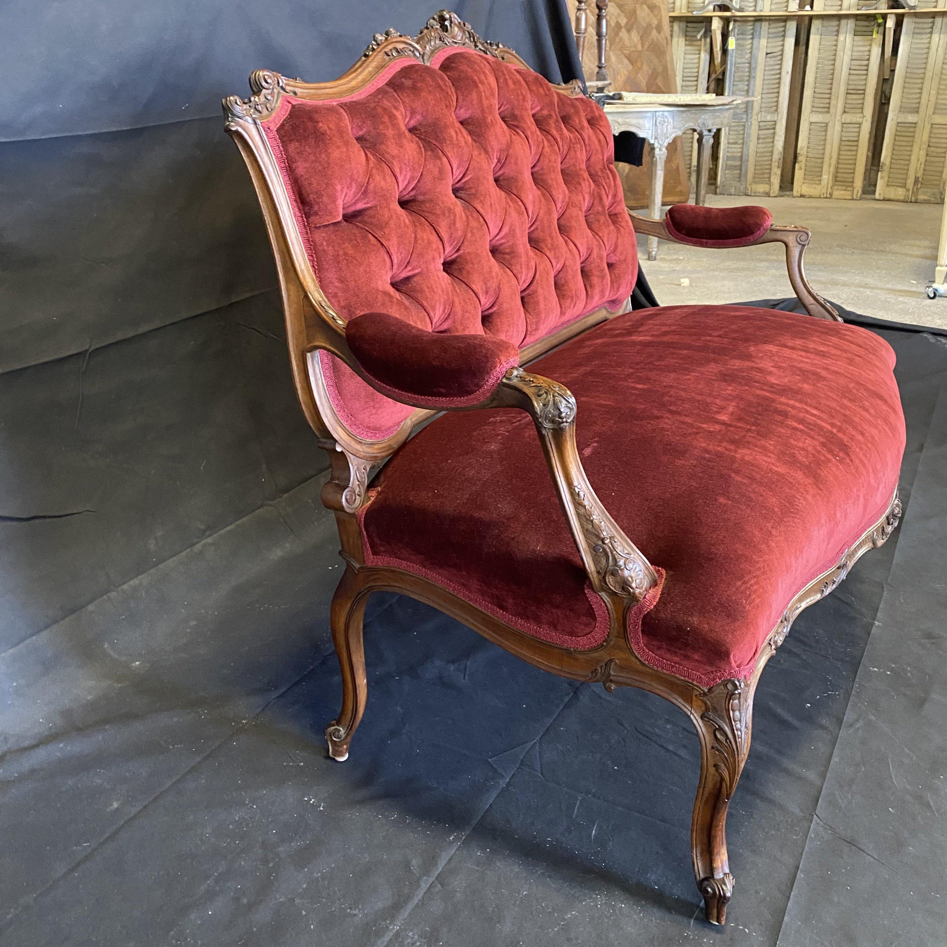 A romantic Louis XV style intricately carved walnut sofa with shaped tufted upholstered backrest leading to scrolled partially upholstered armrests with scrolled floral detailing, Knees have carved acanthus leaves and a diamond carved skirt, central