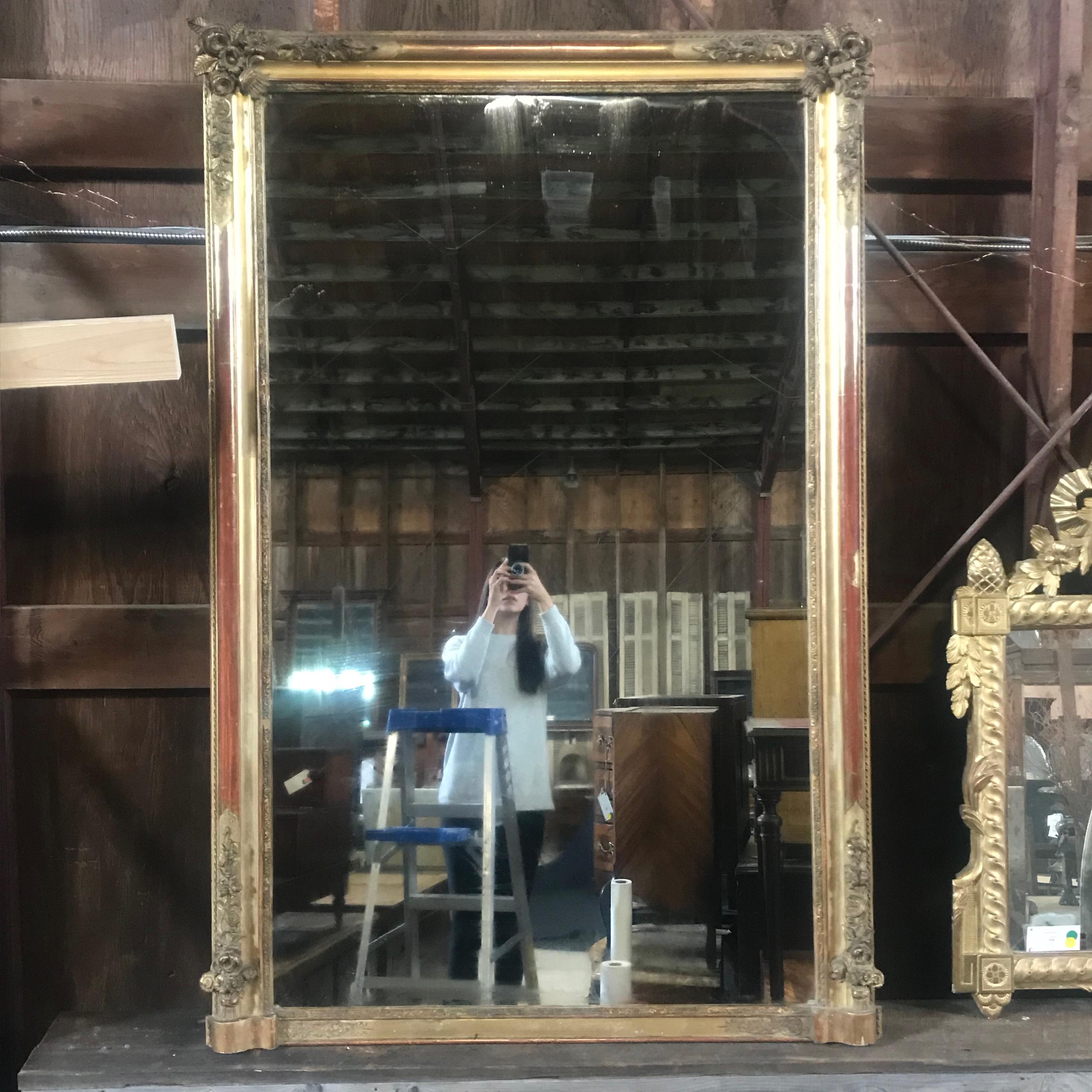 Stunning large French gold carved giltwood mirror with ornate floral design. Re-gilding to the patinated leaf. Antique original paneled wood back.

#3572.