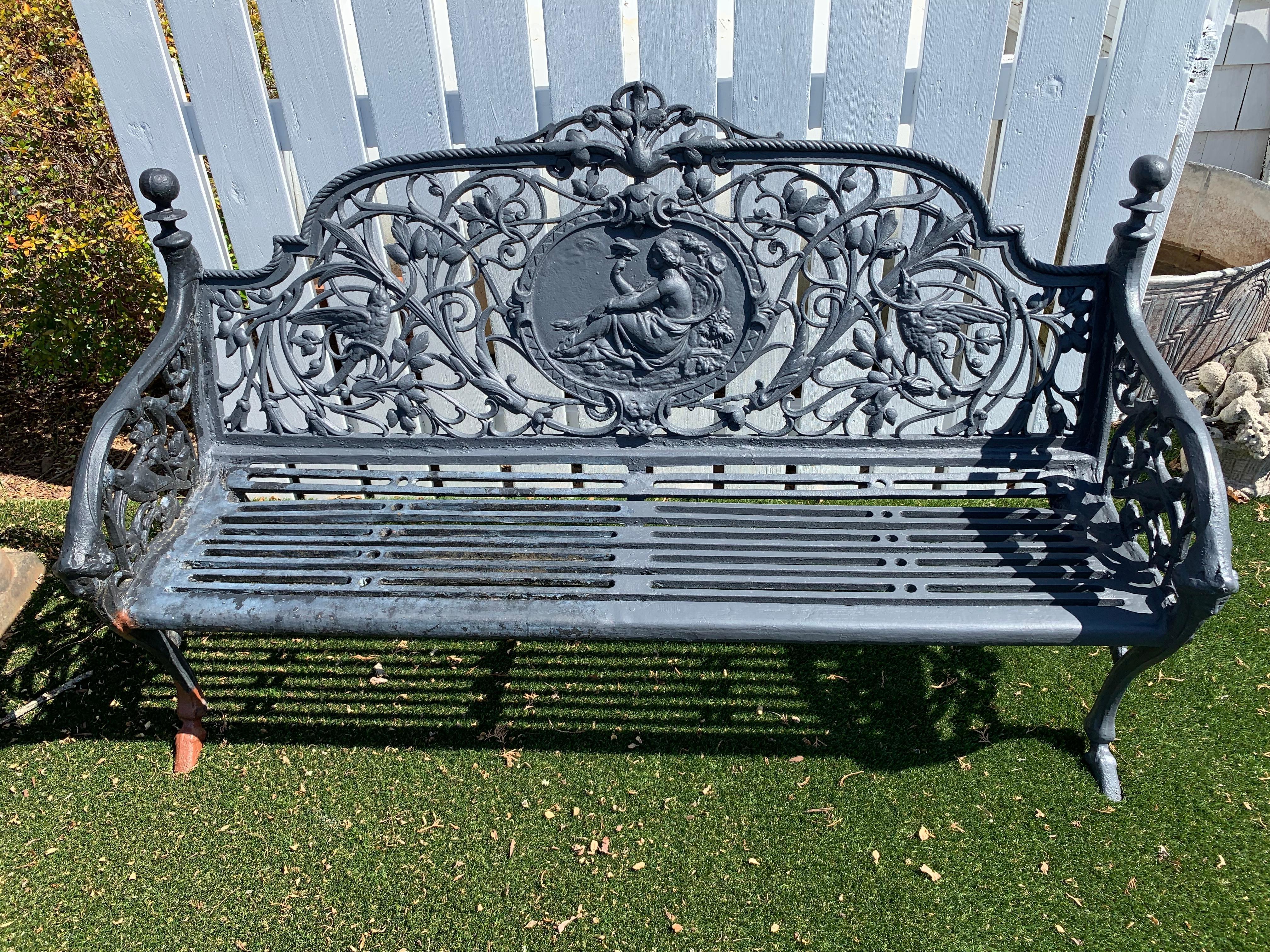 Magnificent vintage black iron bench with ornate decoration having central oval mandala with seated nymph surrounded by intertwining vines, birds, and foliage. Note: Pair available
Measures: arm height 26