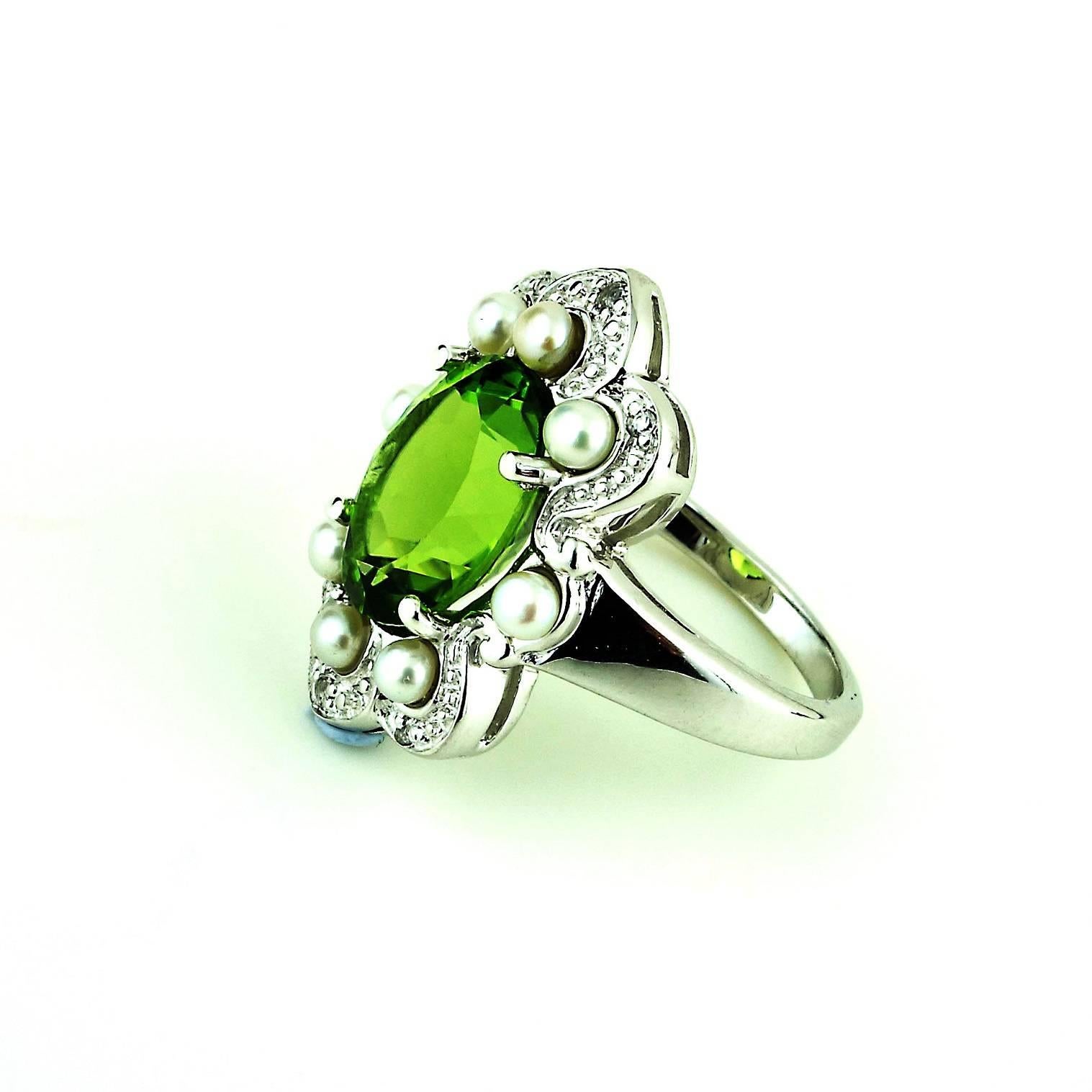 Romantic, unique, flashing oval Peridot, 5.40 cts, set in a rhodium over Sterling Silver ring.  The Peridot is nestled in a larger setting of eight freshwater pearls which are surrounded by sparkling white topaz. It is just under an inch in length. 