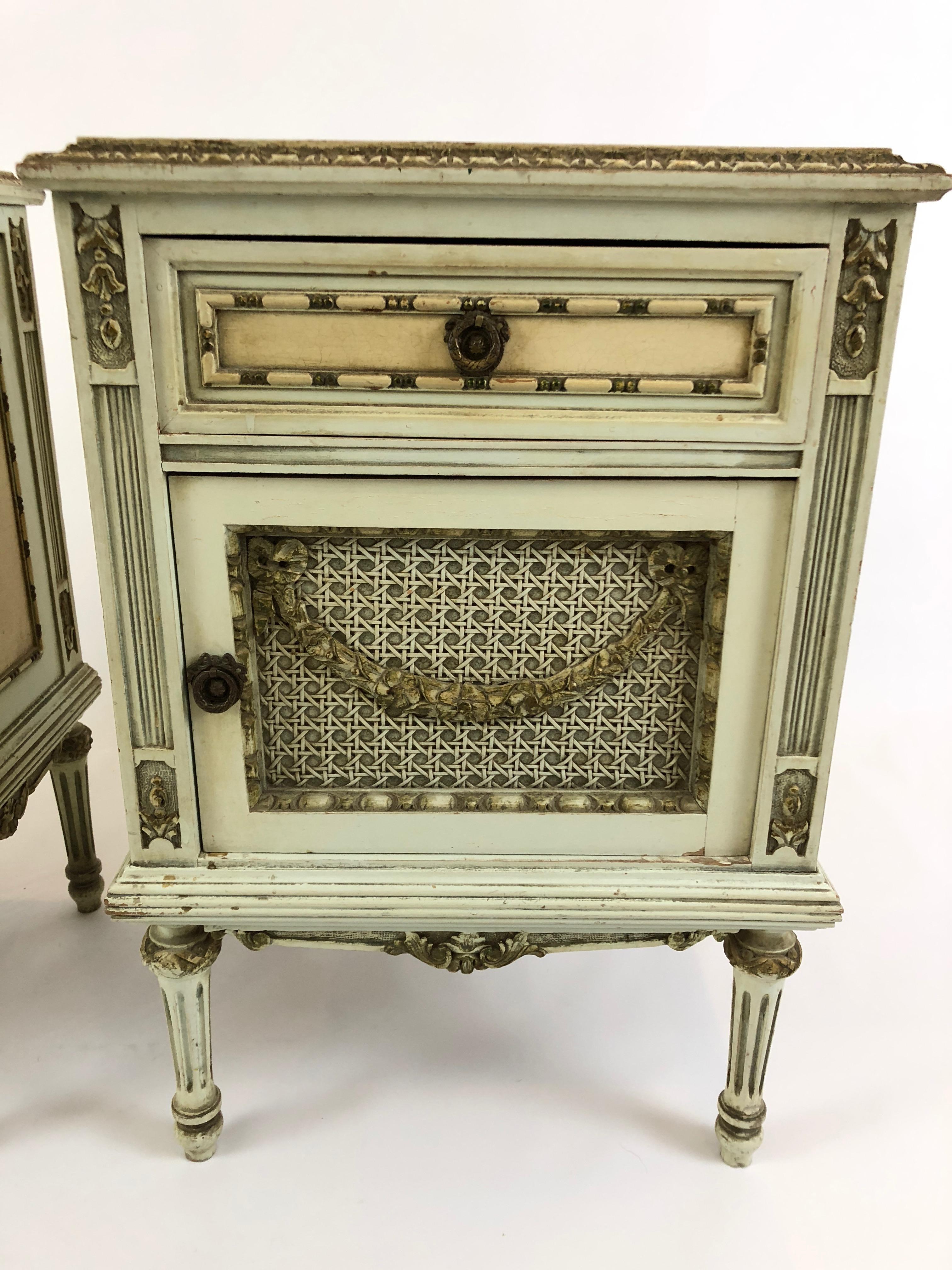 Two very romantic and ornate Louis XV style French nightstands painted a light celadon green, cream and gold, having single drawers and caned panelled doors that open for storage inside.