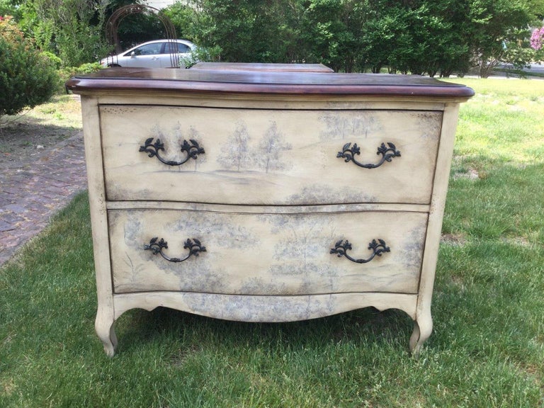 Very decorative pair of chinoiserie inspired commodes having deep clean drawers and natural wood tops. The background color of the chests can be described as antique white while the soft landscape decoration is light gray sepia. The design is very