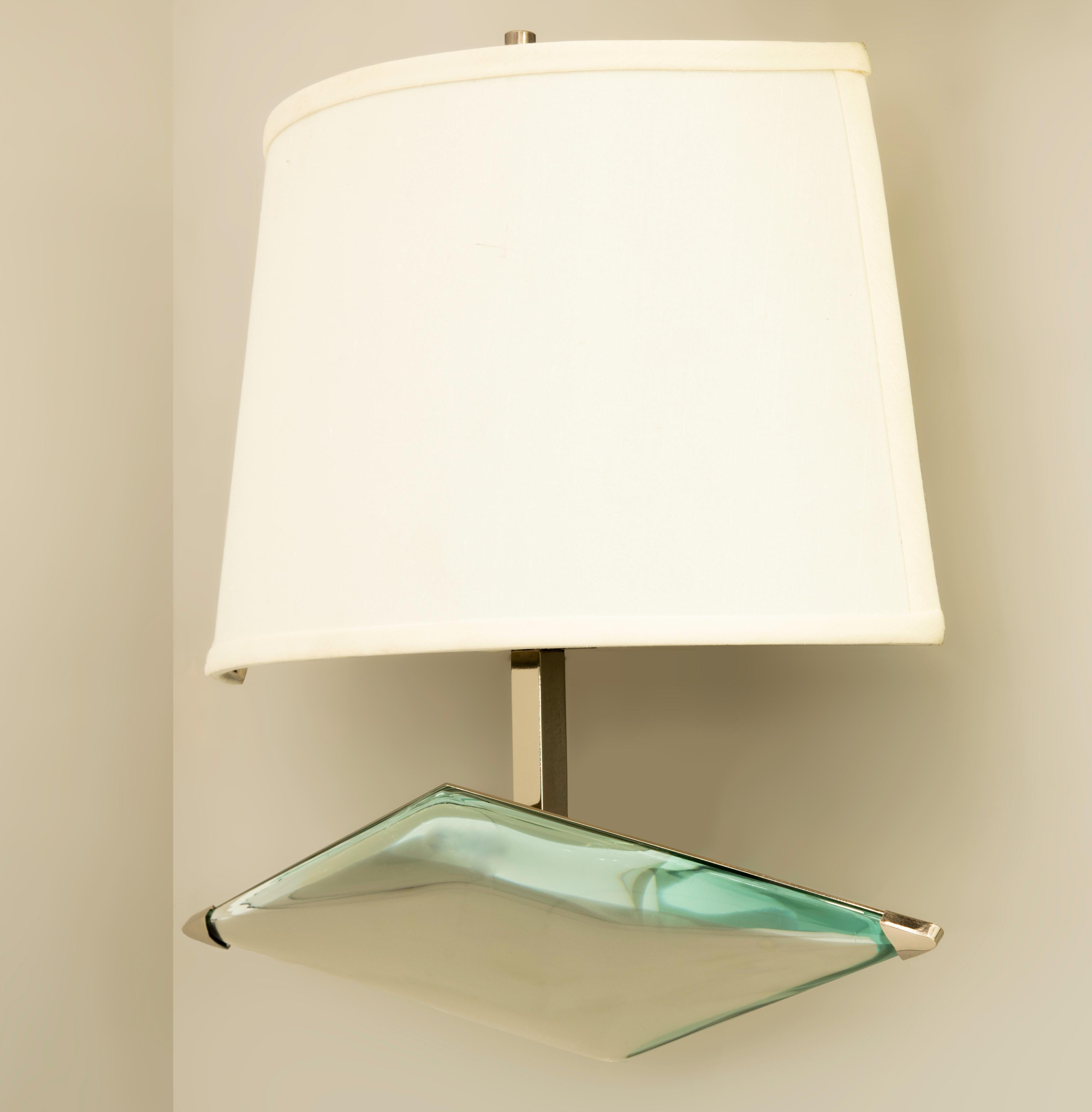 The Rombo wall light by form A is designed around a thick starphire glass which has been hand carved in the shape of rhombus. Mounted on a sloping frame ending with a frosted glass or silk shade. Shown in polished nickel with a silk