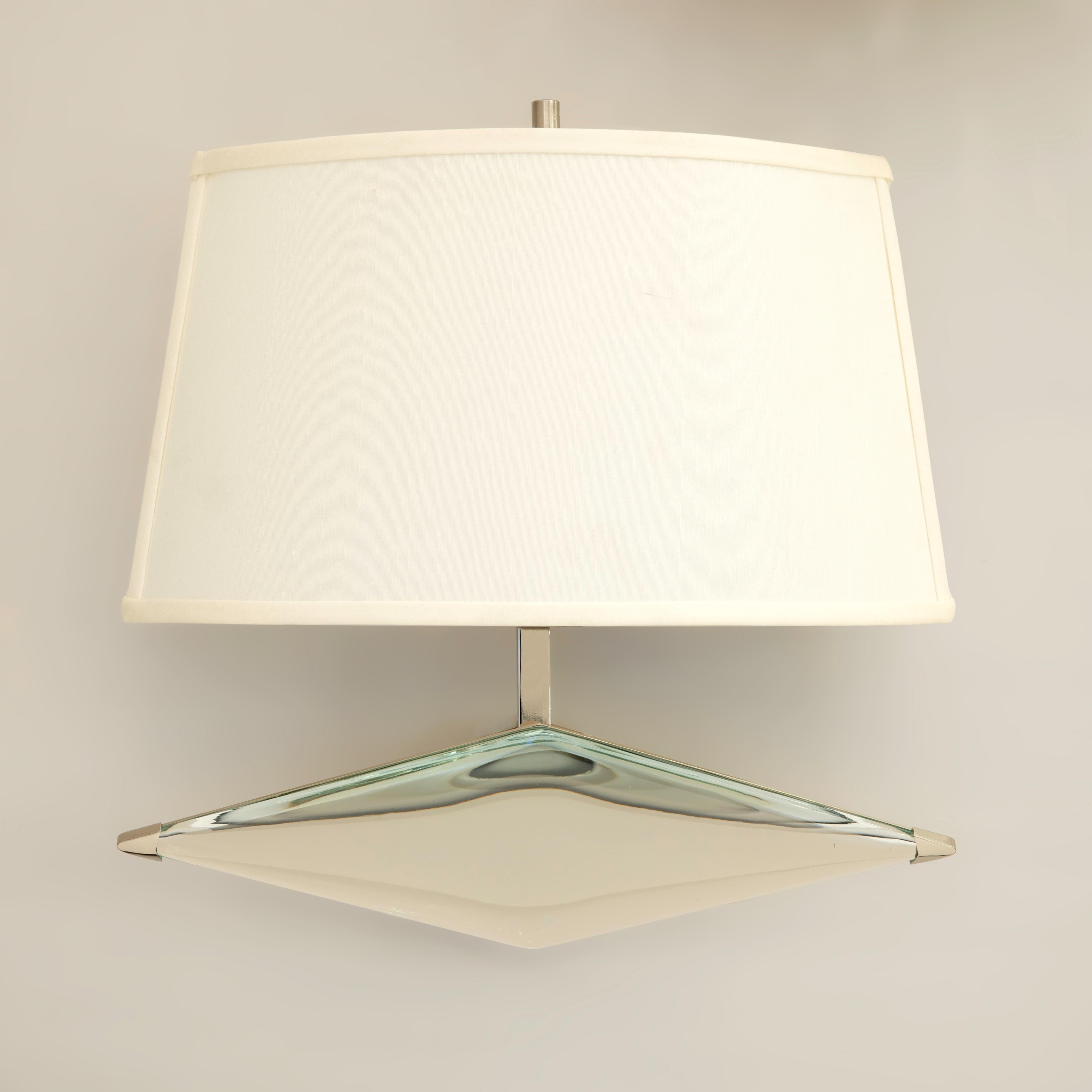 The rombo wall light is designed around a thick starphire glass which has been hand carved in the shape of rhombus. Mounted on a sloping frame ending with a silk shade. Shown in polished nickel. Listed price is for the stock model in polished