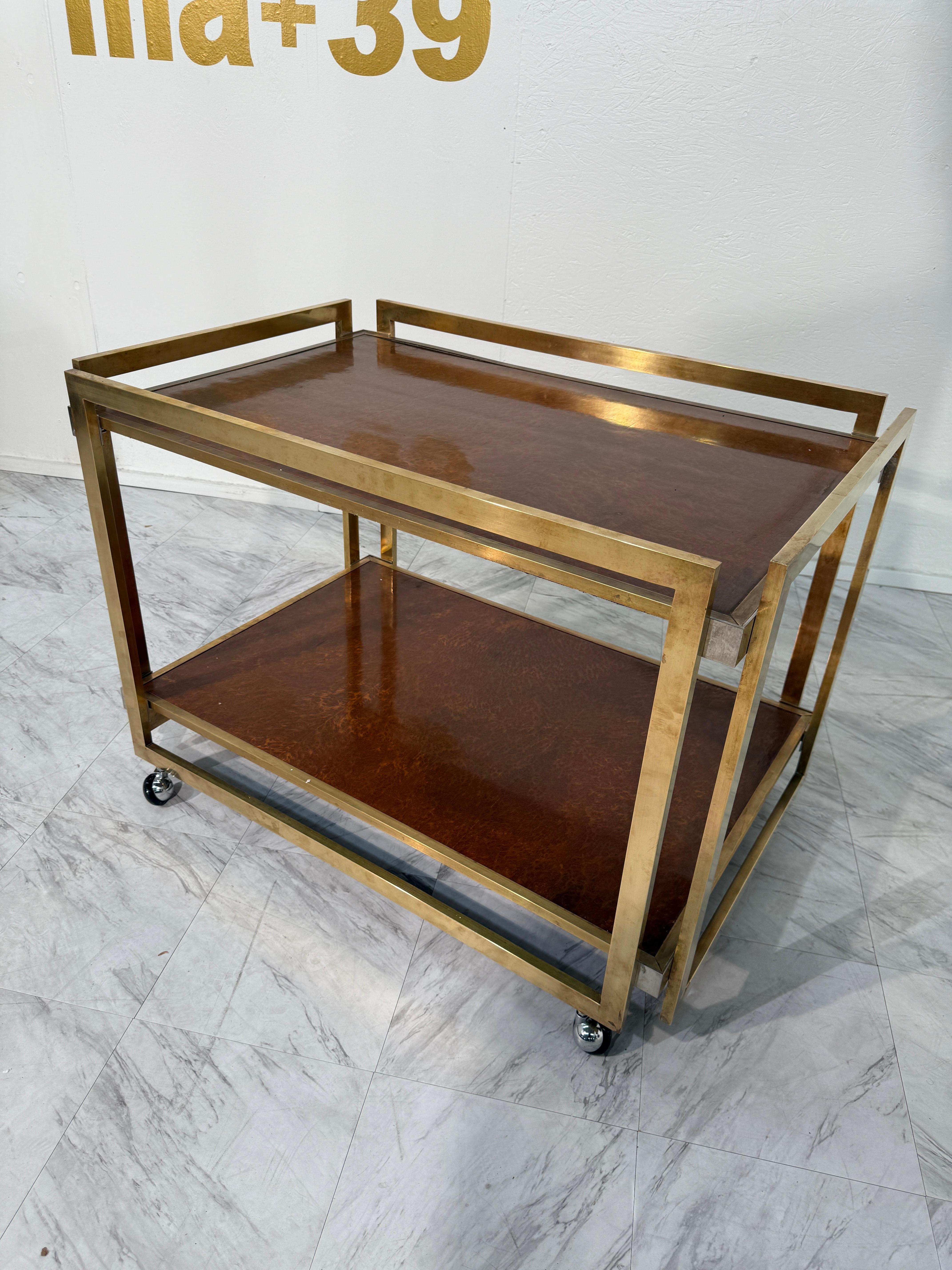 Carrello da bar degli anni '70 di Romeo Rega, che combina un'elegante struttura in ottone con ripiani in legno di radica. Il design a due livelli offre uno spazio generoso per esporre bicchieri, bottiglie o oggetti decorativi, mentre la struttura