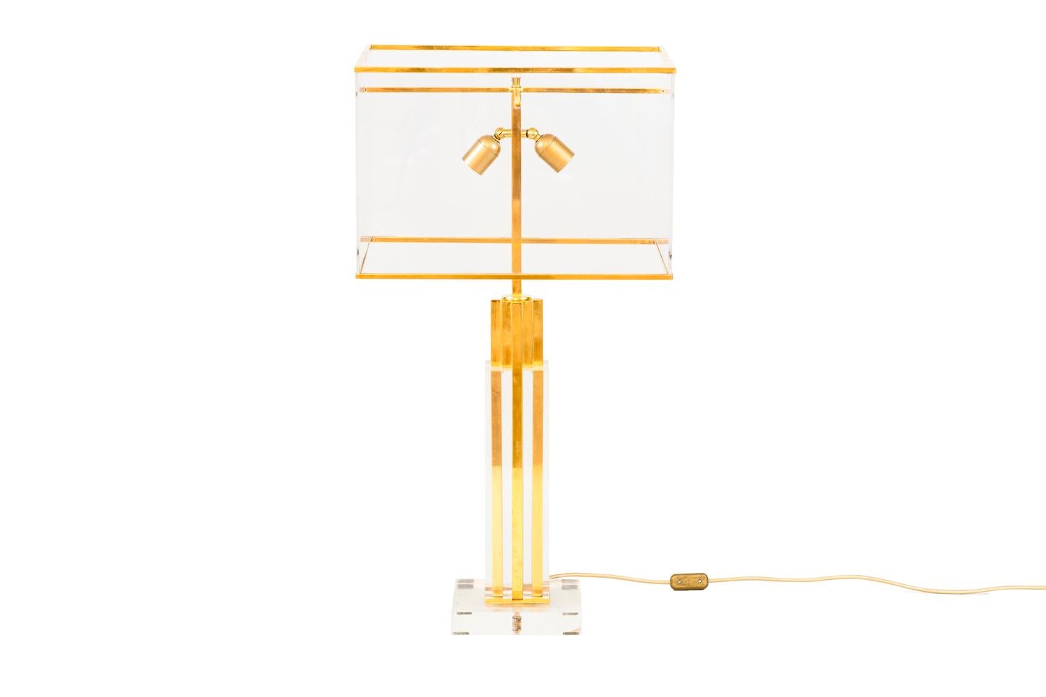 Romeo Rega, in the style of.
Column lamp standing on a Lucite square base. Gilt brass shaft framed by Lucite parts.
Rectangular lamp shade in Lucite with gilt brass support.

Work realized in the 1970s.

New and functional electrical