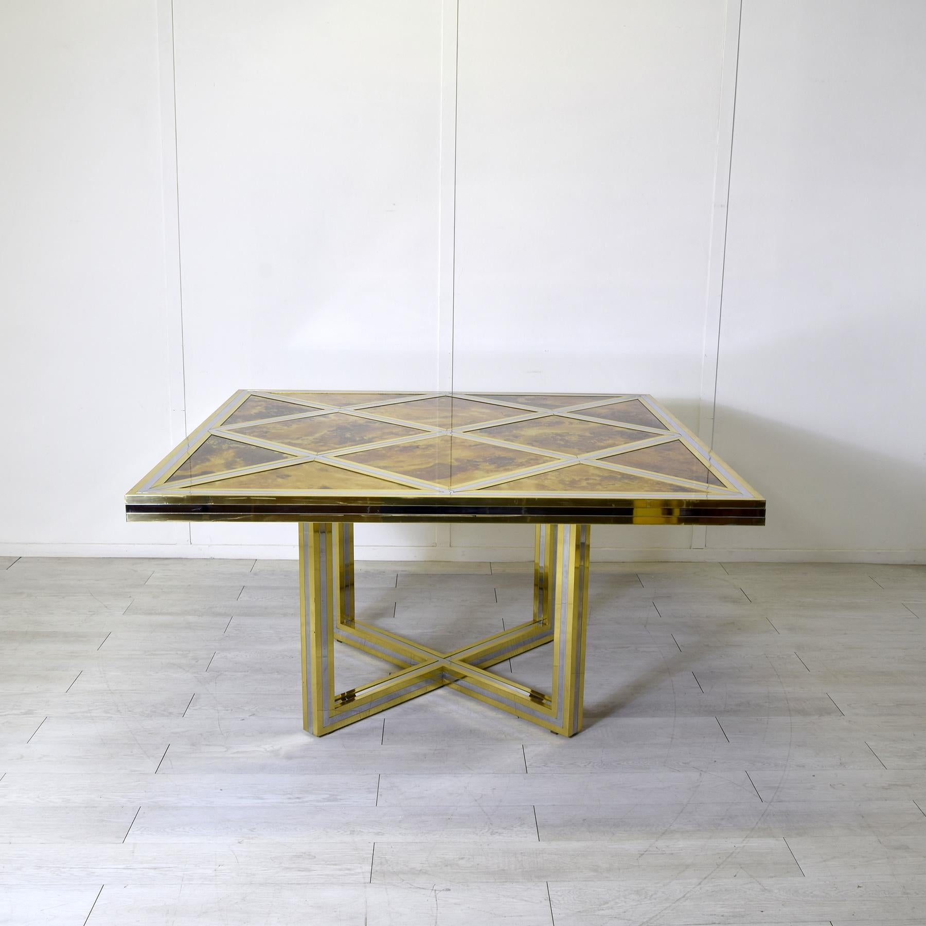 Elegante tavolo in ottone con struttura dorata e nichelata, sul piano una serie di riquadri ne definiscono la precisa forma geometrica, completata da elementi incastonati in metacrilato effetto tartaruga tipico della fine degli anni Settanta. Il