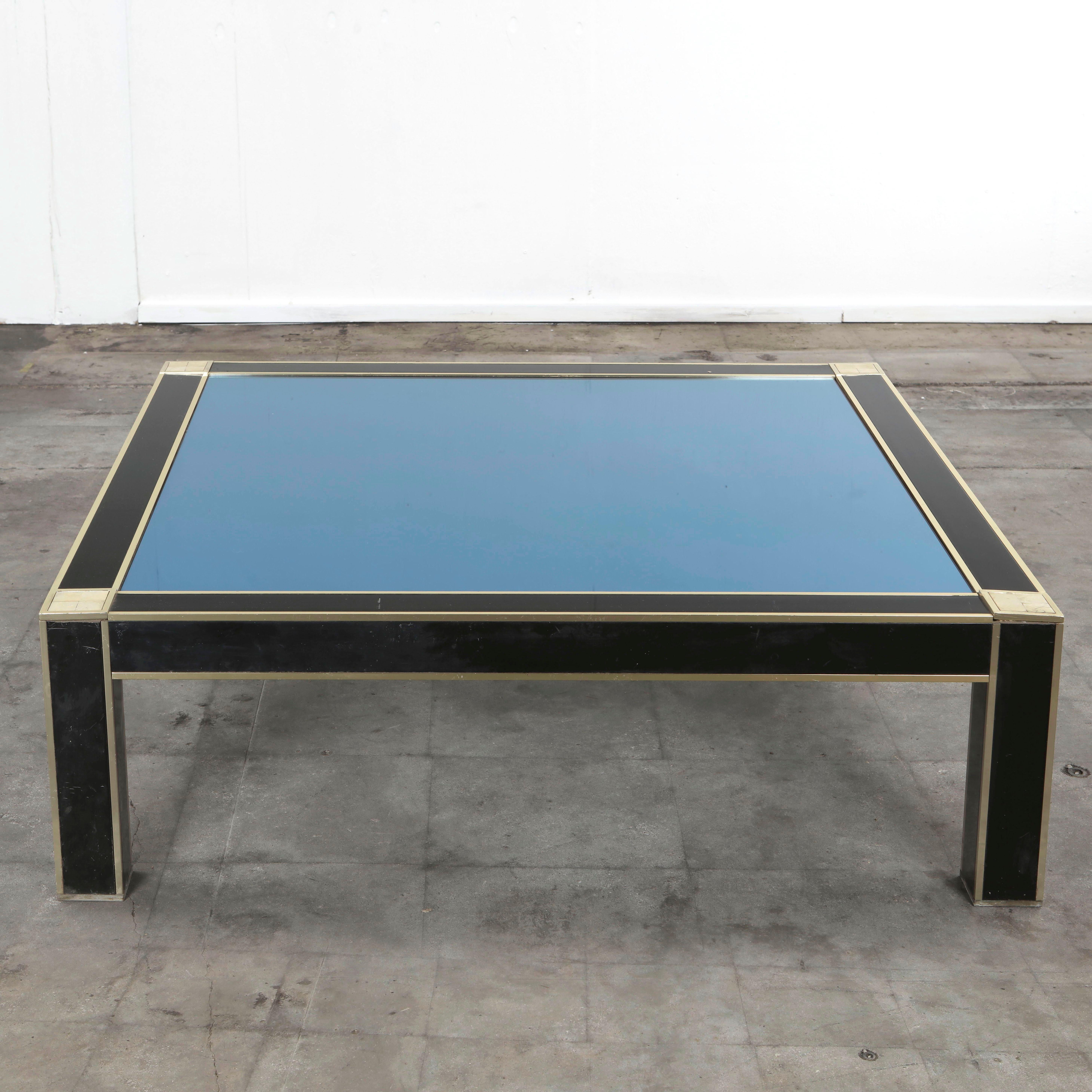 Chic Italian modern coffee table from the 1970s featuring a bold geometric composition in black lacquer, brass, and glass. The square frame, edged with brass trim, encloses a top in deep blue glass that catches and reflects light with elegant depth.