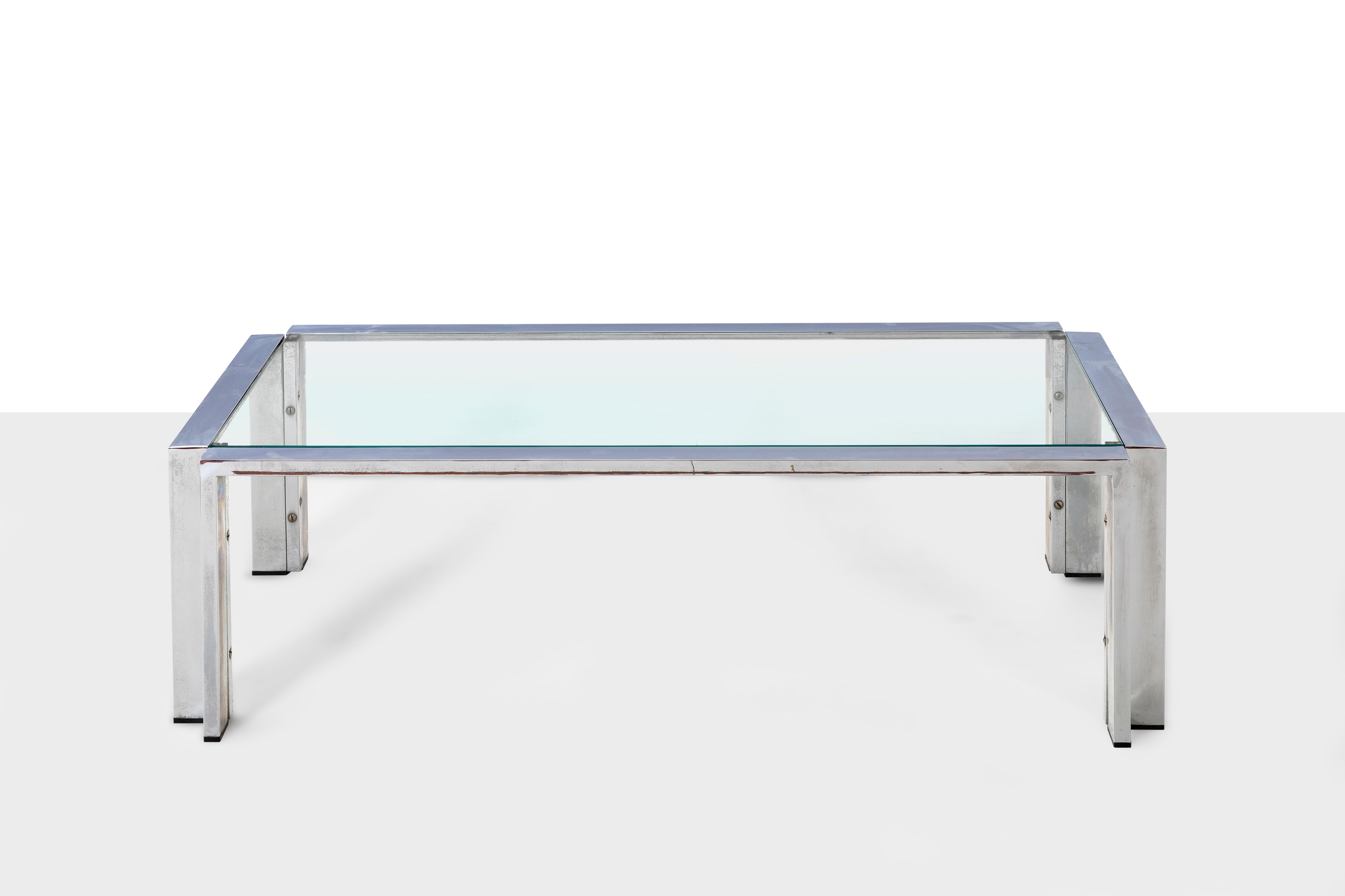 Low lounge table in steel and beveled glass top. The special feature of the table is the shape of the legs that create a concave angle. It is a coffee table that is easily adaptable to both a living room and a study, and also in a waiting room. Its