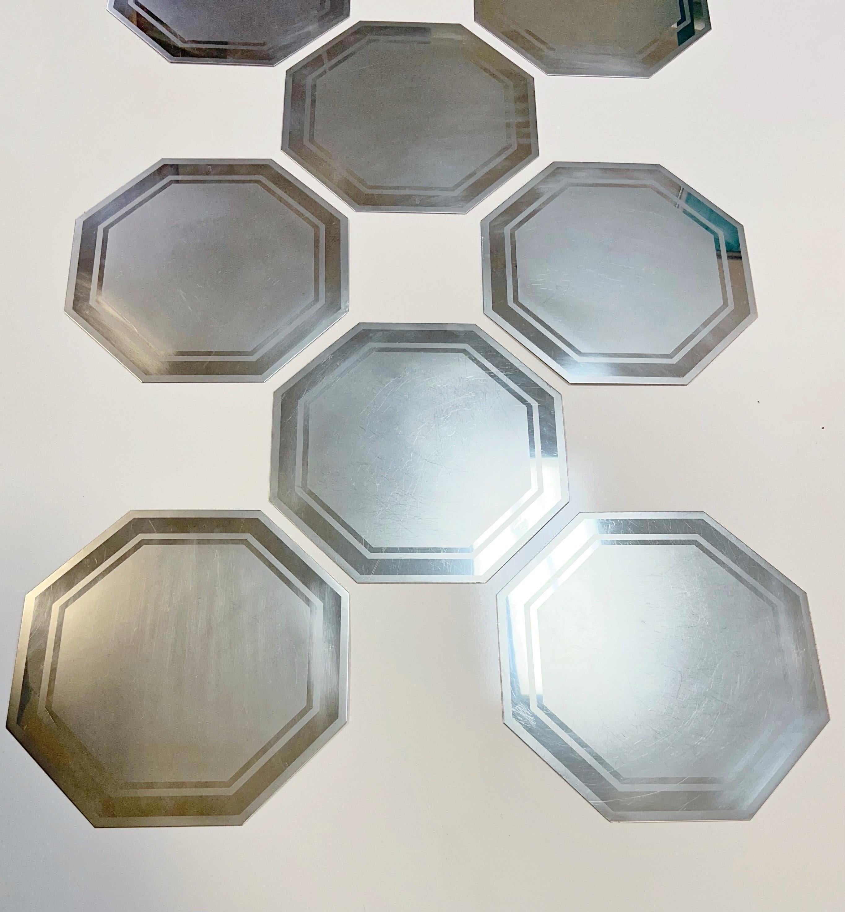 A rare set of 8 modern placemats by Romeo Rega. Octagonal in shape. The surface has a geometric design in polished stainless and mate. All are signed. In good condition showing scuffing from age and use.