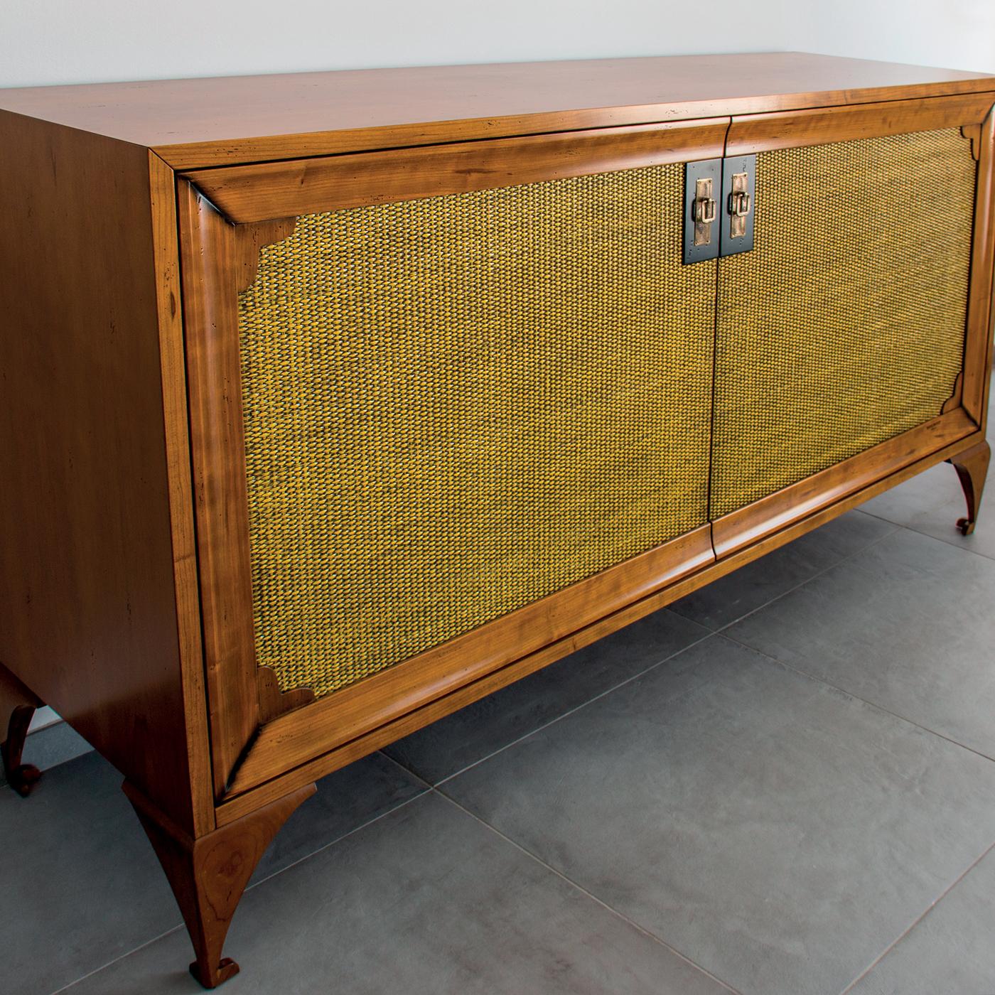 This sideboard is exquisitely crafted of solid cherrywood, and enriched on the two door-panels with a pale yellow canette piqué fabric with a lovely ribbed texture. The internal storage features drawers and two shelves on each side, allowing for