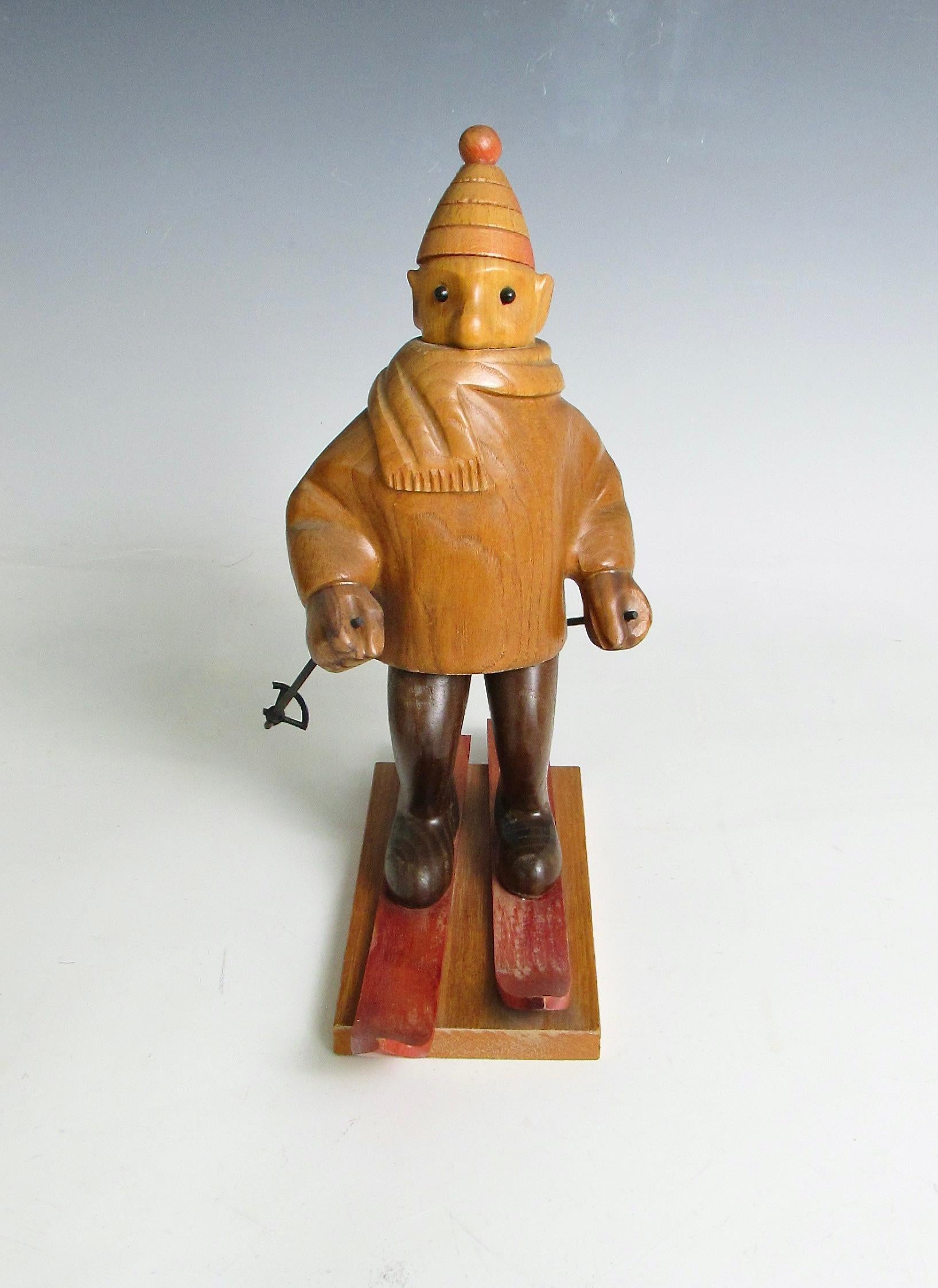 Skurrile geschnitzte Figur eines Abfahrtsläufers. Eingemummelt mit Mütze und Schal . Skistöcke in der Hand. Ein Korb am Skistock beschädigt.   . Handgeschnitzt in Italien Ende der 1960er bis in die siebziger Jahre. Dies ist eine von vielen