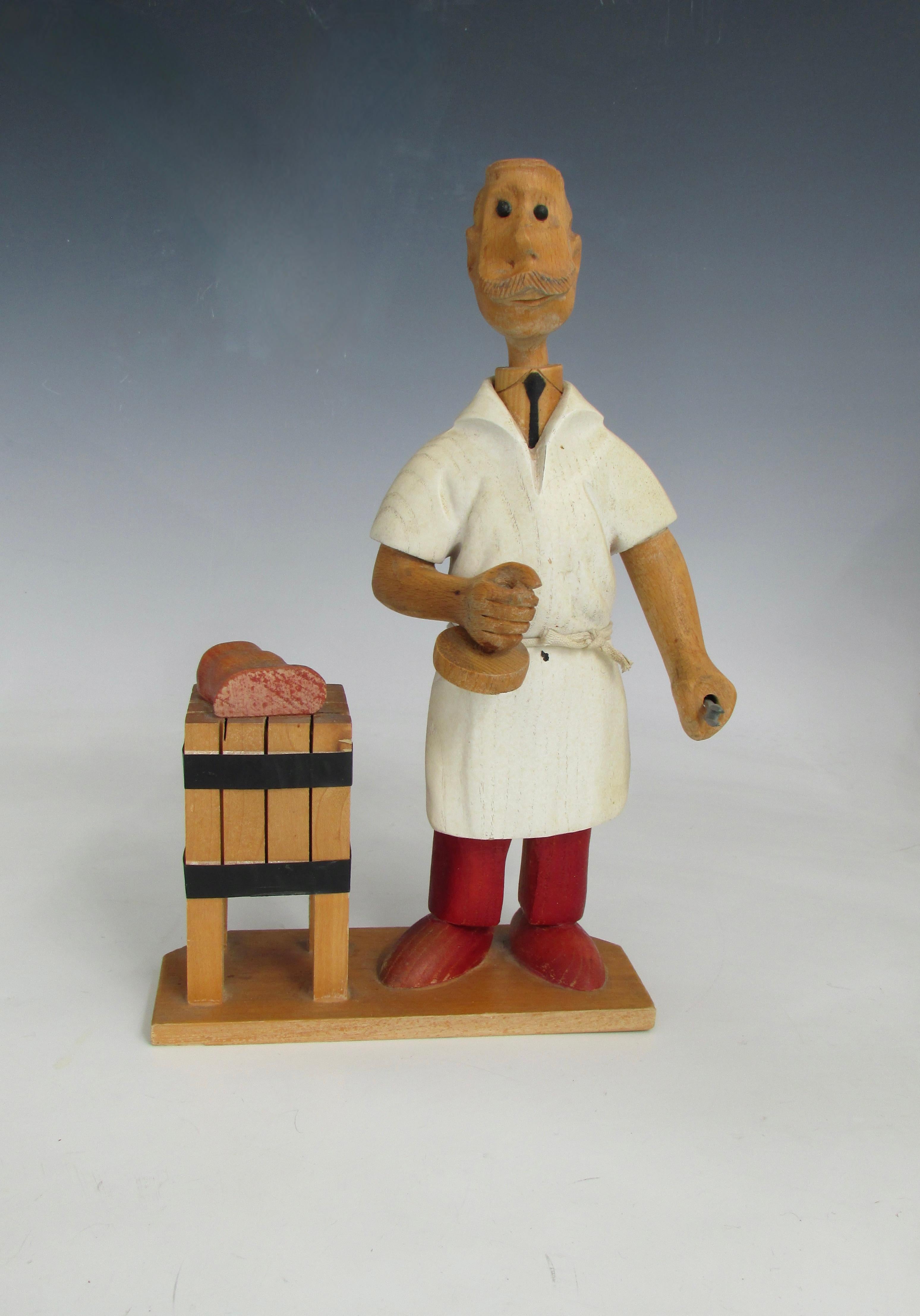 Caprichosa figura tallada de un carnicero con delantal blanco trabajando en una mesa de carnicero  . Tallado a mano en Italia de finales de los 60 a los 70 . Esta es una de las muchas figuras talladas que representan oficios y aficiones .  Fabricado