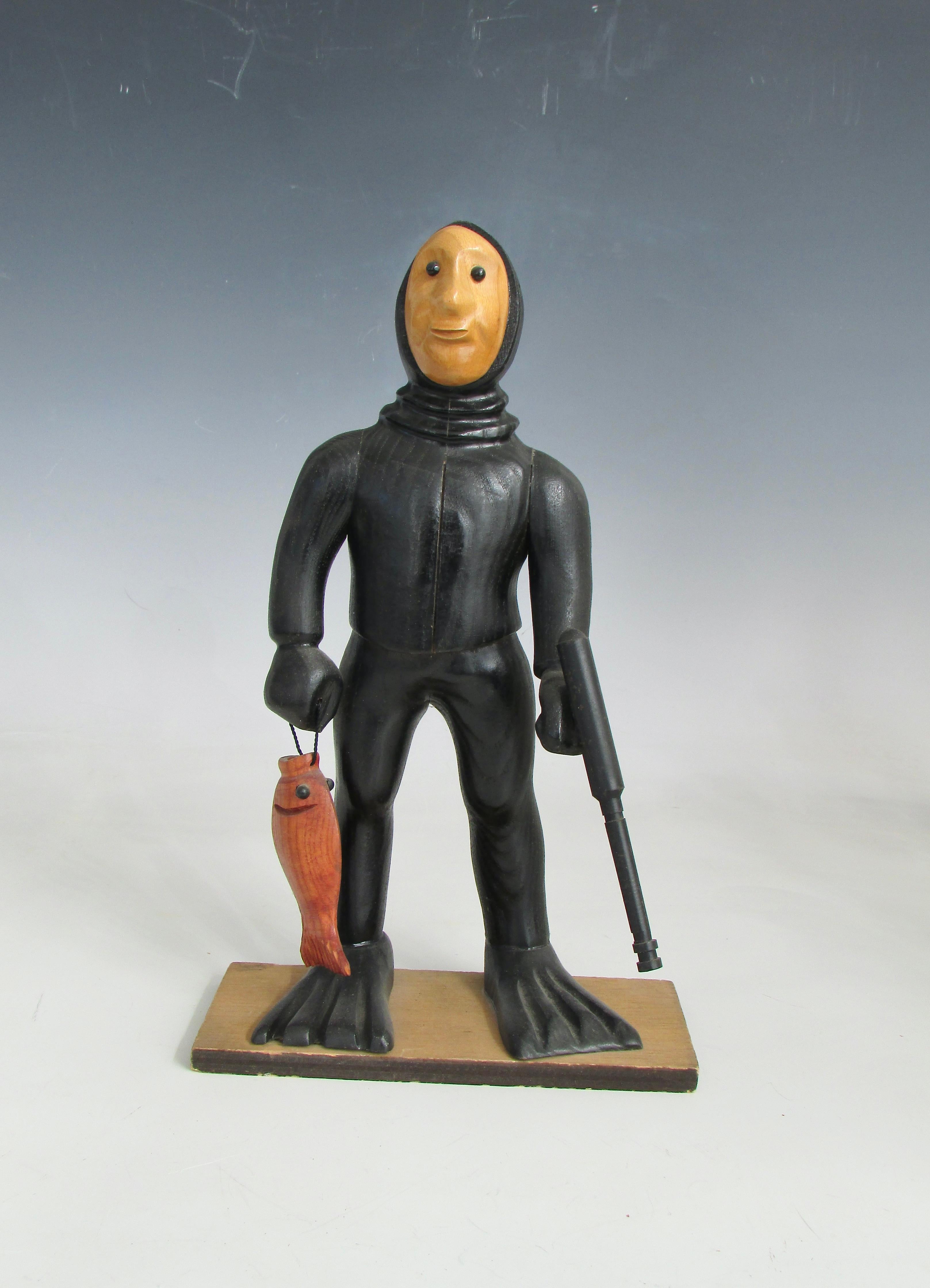 Caprichosa figura tallada de buceador de piel , pescador con arpón . Enfundado en traje de neopreno con fusil submarino y pesca fresca . Tallado a mano en Italia de finales de los 60 a los 70 . Esta es una de las muchas figuras talladas que