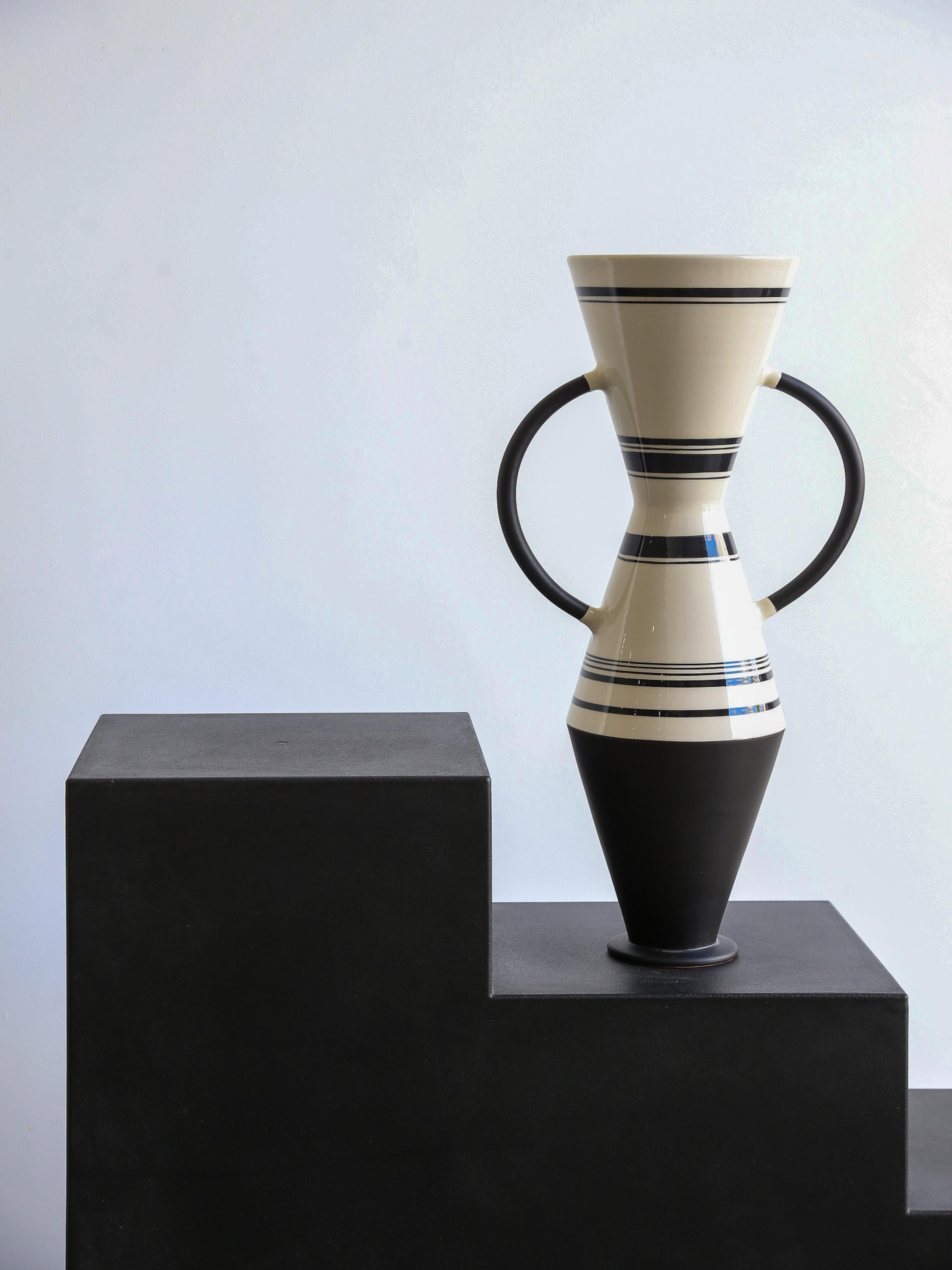 Conical and spheroidal vases play with lines and crosses in a black and white ritual. Clay vase, hand thrown, with clay handles. Matte black glaze finish for the base and handles, white engobe decorated black with transparent glaze for the