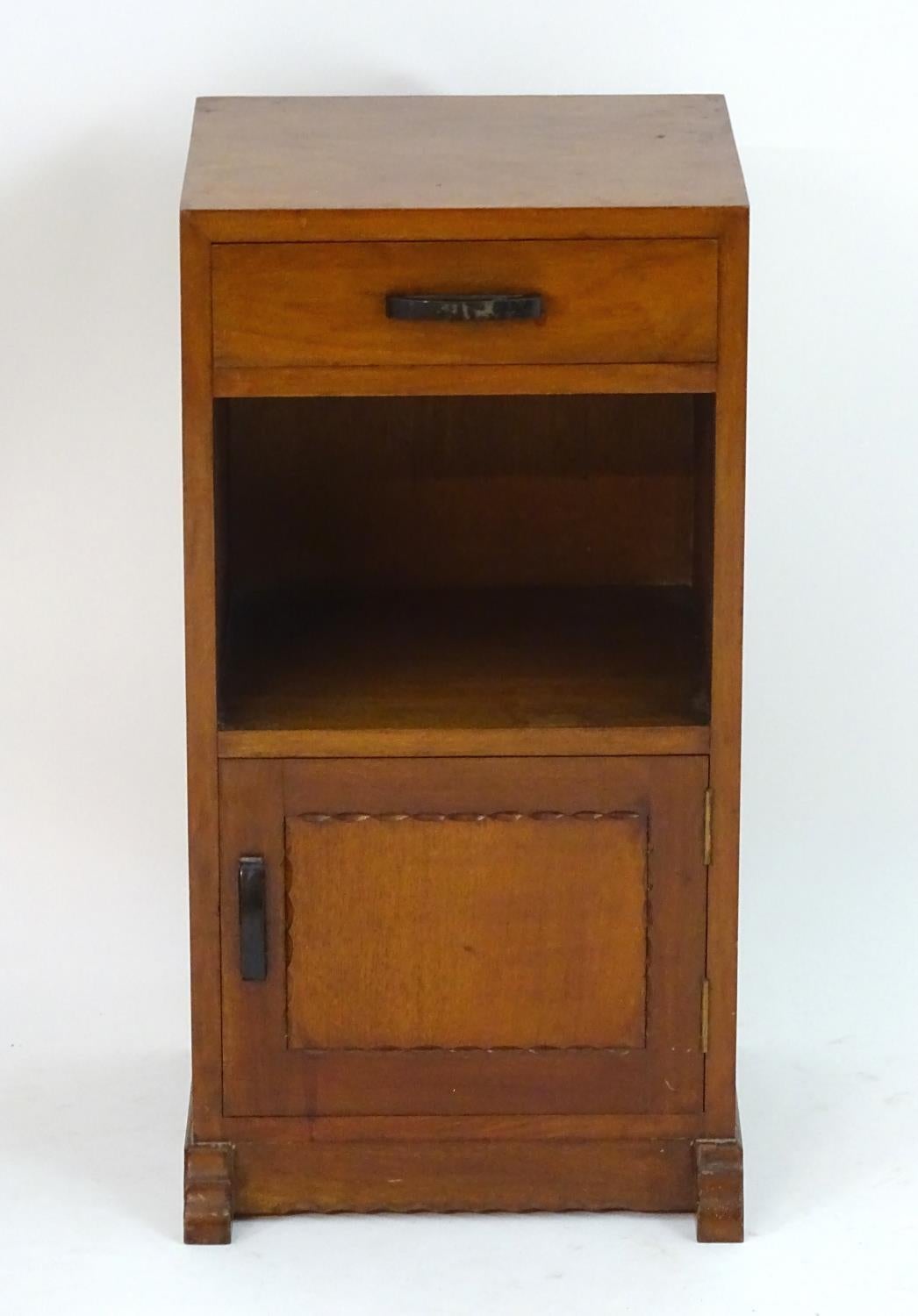 Romney Green, in the style of.
An Arts & Crafts Cotswold School walnut bedside cabinet with a single drawer, an open area below and a chip carved door with ebonized handles, on shaped feet with a subtle carved details.