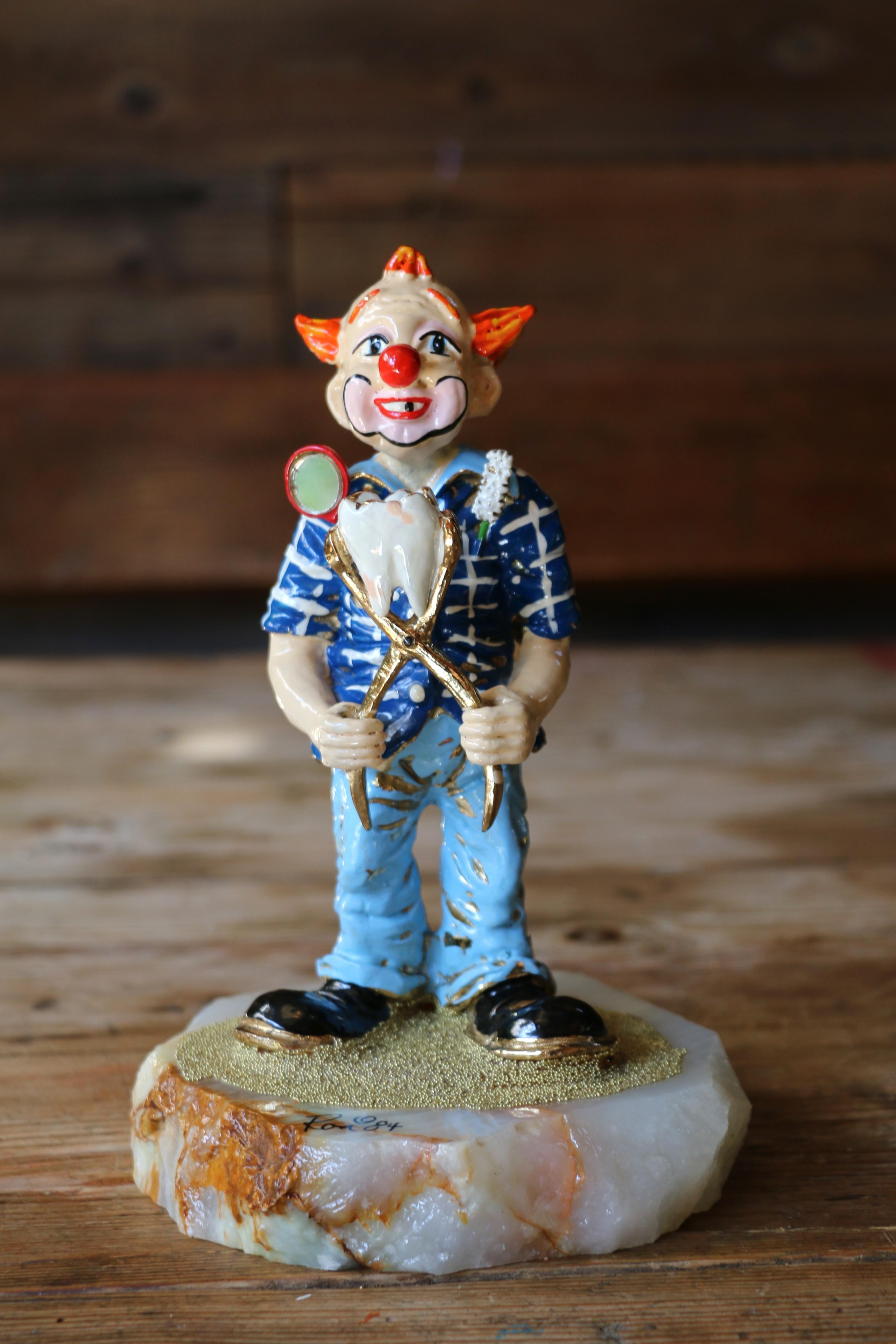 Bellissima statuetta vintage da collezione realizzata dall'artista americano Ron Lee nel 1984. Questa scultura raffigura un clown che tiene un grosso dente estratto con delle pinze, giocando sul tema dell'odontoiatria in uno stile stravagante.
