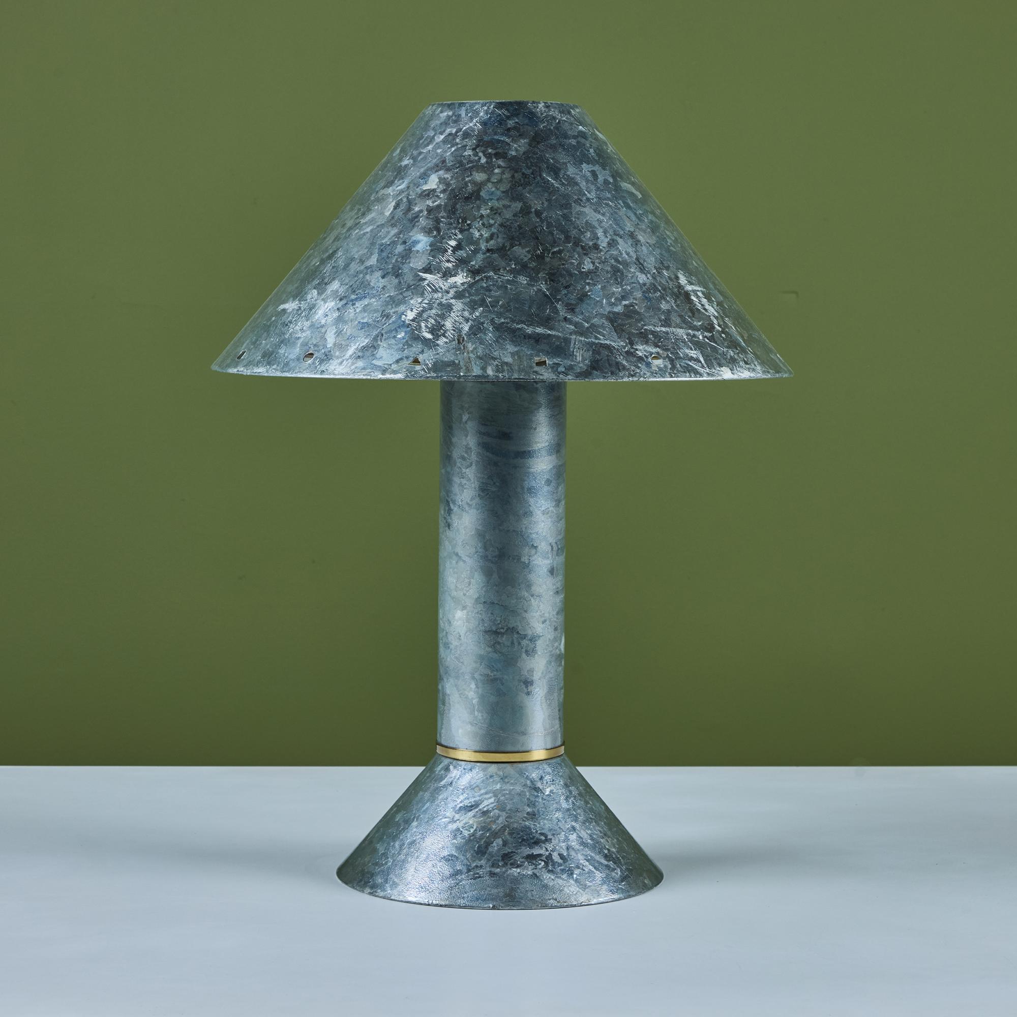 Postmodern table lamp by Los Angeles lighting designer Ron Rezek, c.1980s. The lamp features a galvanized steel frame and removable steel shade with polished brass ring accent that sits at the top of cone shaped base. The shade features different