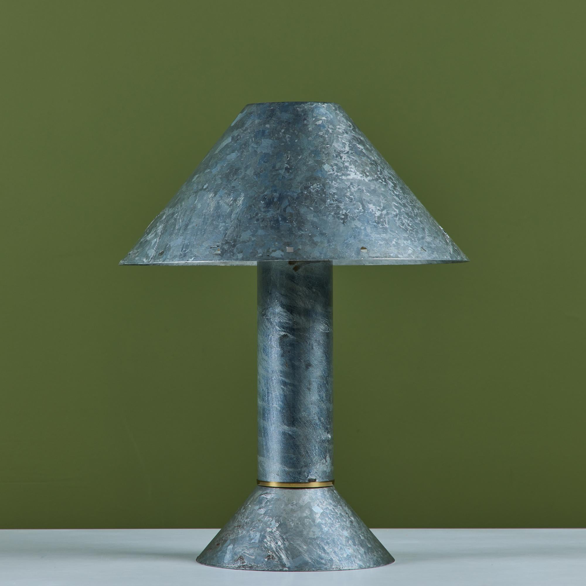 Postmodern table lamp by Los Angeles lighting designer Ron Rezek, c.1980s. The lamp features a galvanized steel frame and removable steel shade with brass ring accent that sits at the top of cone shaped base. The shade features different shaped