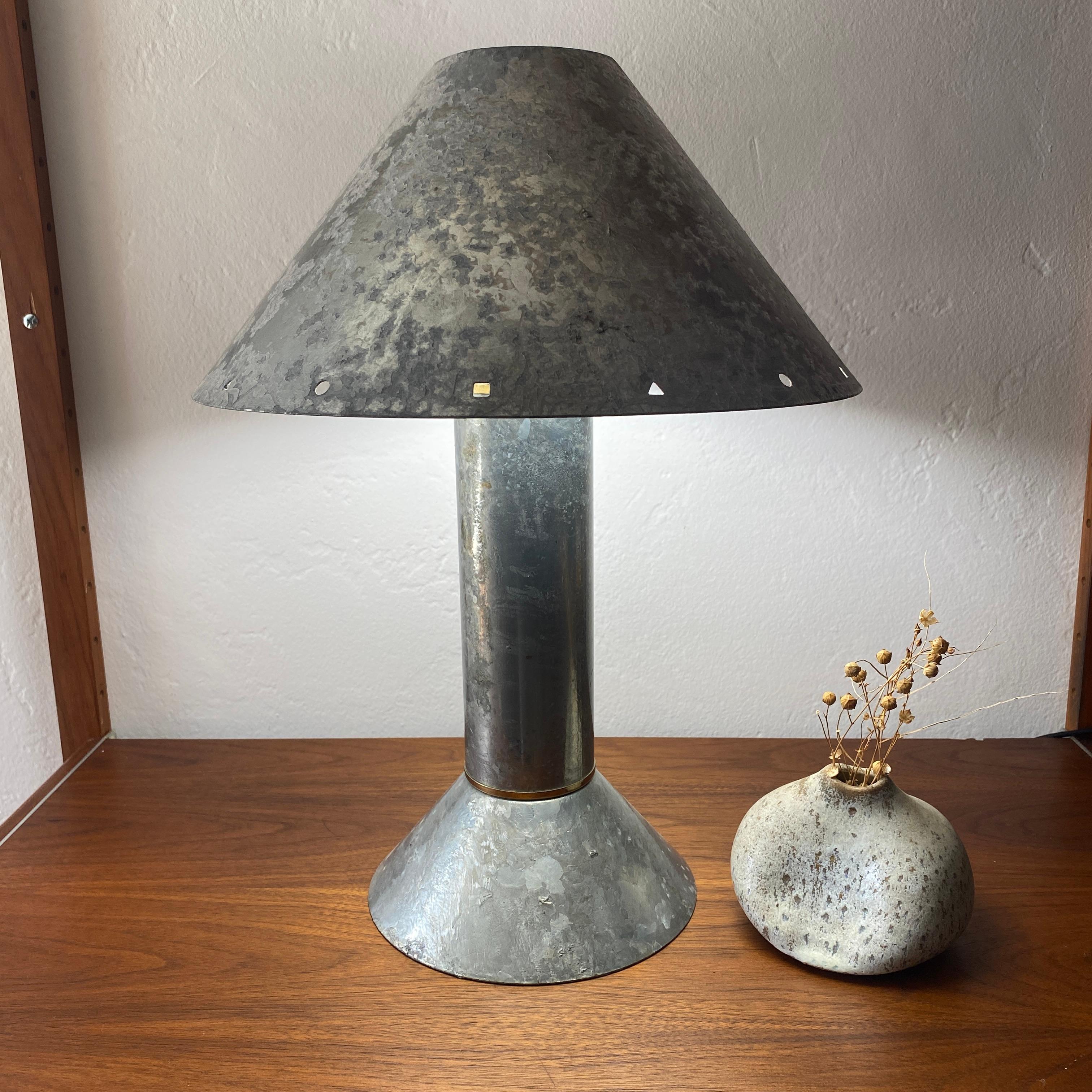 Postmodern table lamp by Los Angeles, California lighting designer Ron Rezek, c.1980s. The lamp features a galvanized steel frame and removable steel shade with a polished brass ring accent at the top of a cone-shaped base. The shade features