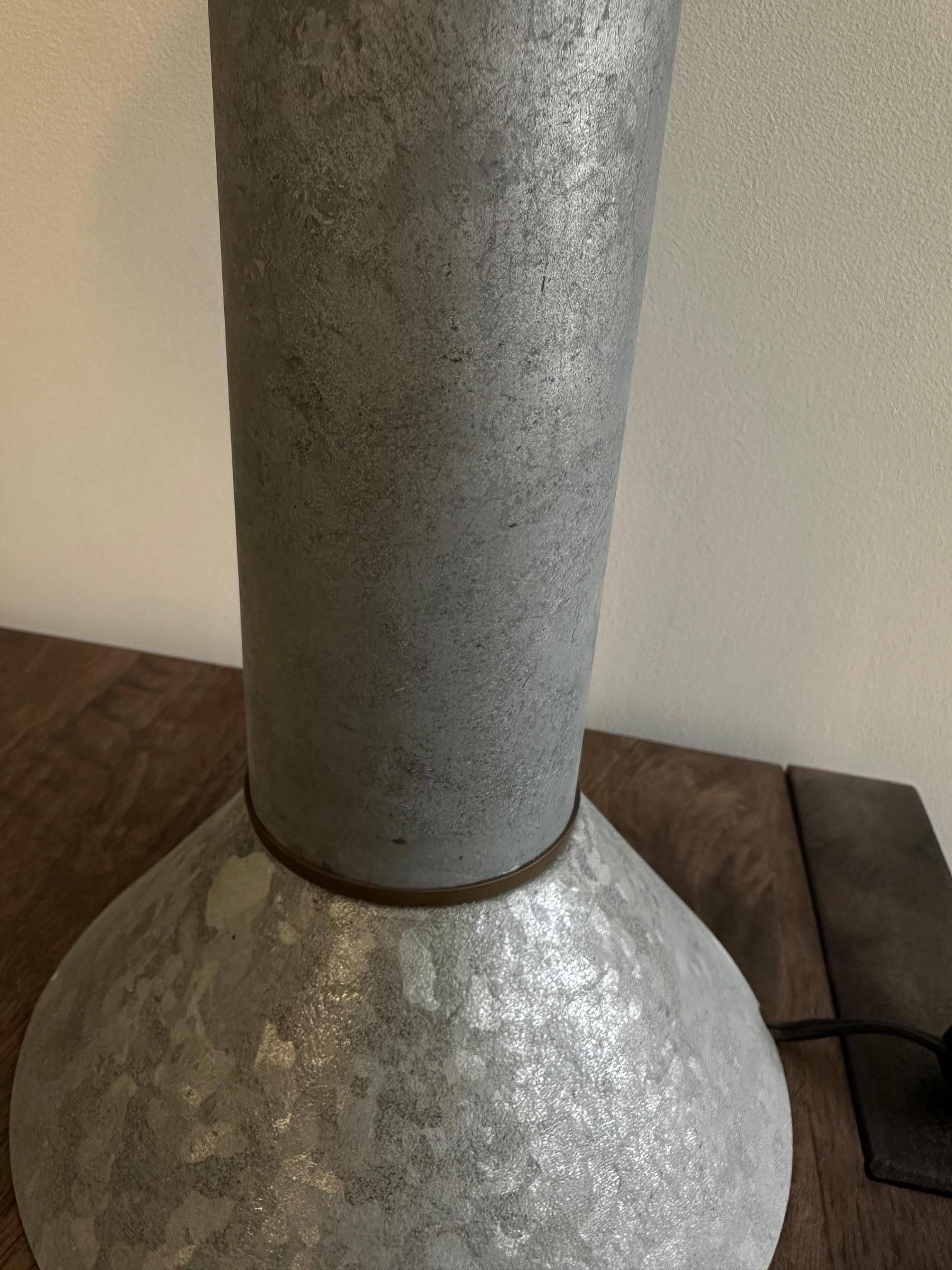 A rare table lamp designed by Ron Rezek, a famed industrial designer, circa 1980s. It is constructed with patinated Zinc and brass accent, reminiscent of the zinc tables designed by John Dickinson. The shade is adorned with cutout to allow the light