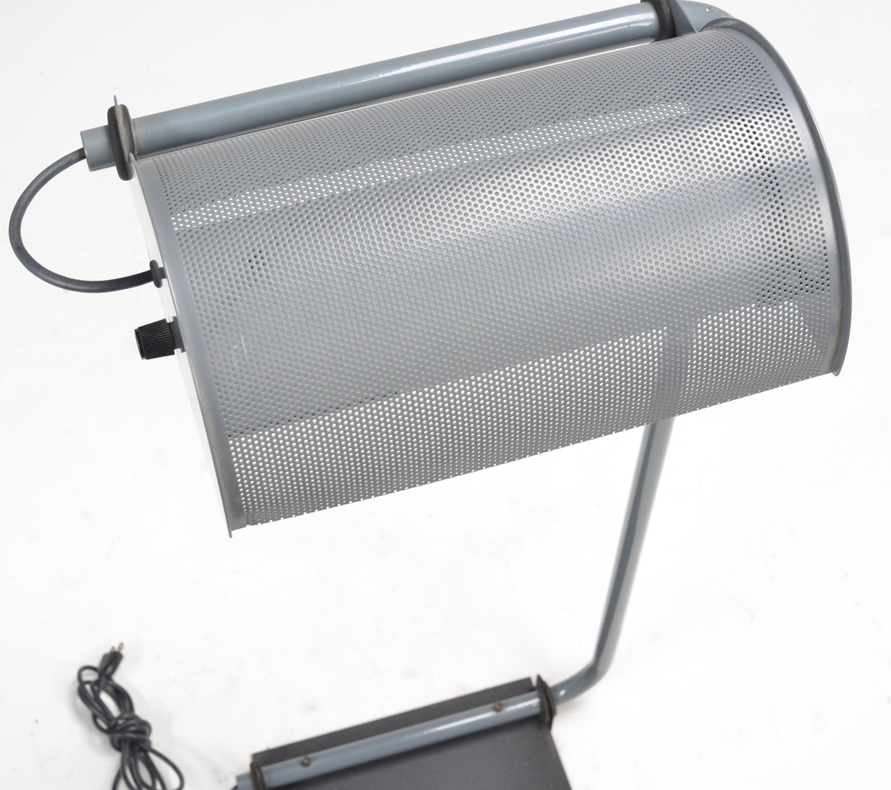 Lámpara de pie arquitectónica de Casella Lighting, San Francisco, con una pantalla semicilíndrica perforada que gira sobre un armazón minimalista de aluminio con base lastrada. El diseño tiene una iluminación limpia y direccional, con materiales