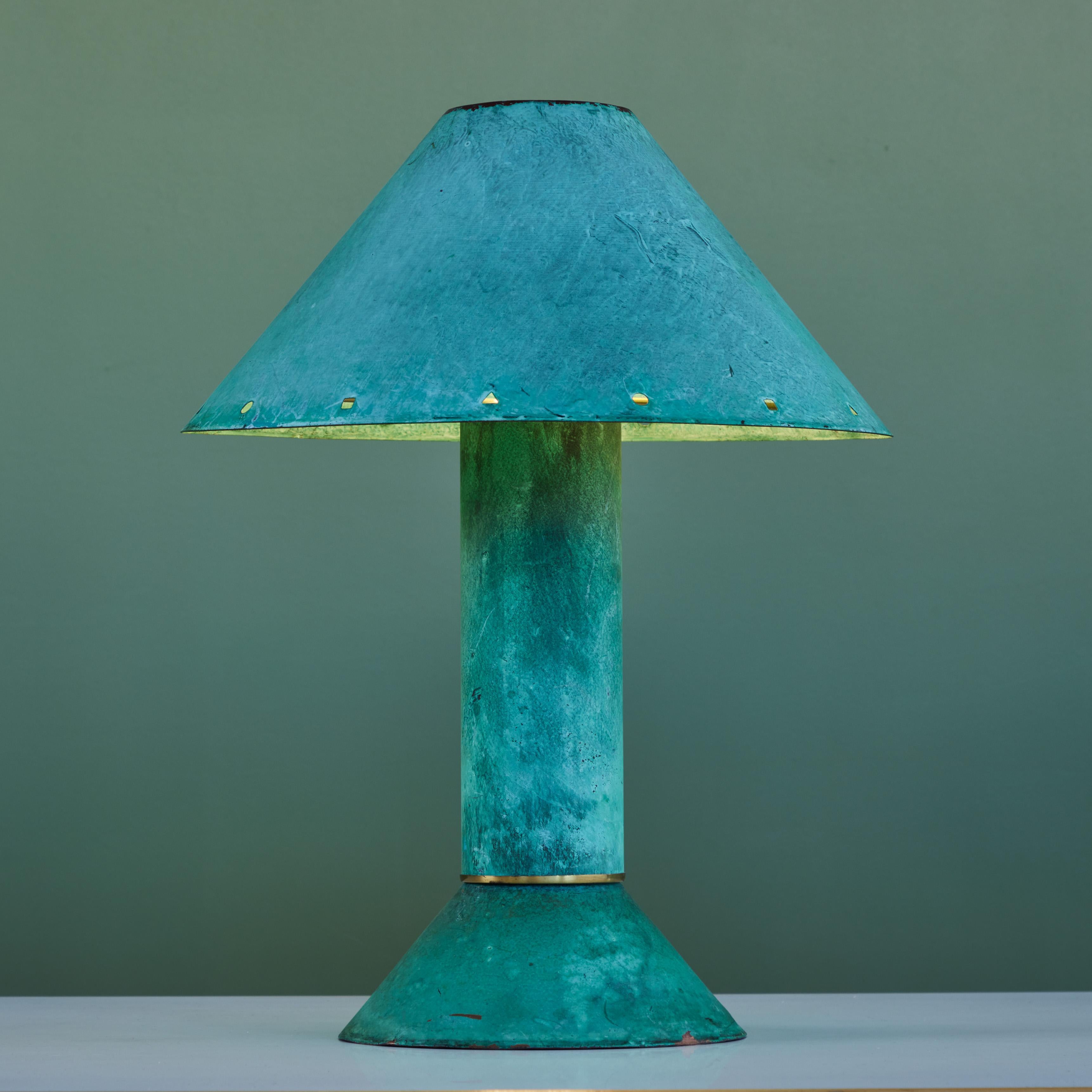 Postmodern table lamp by Los Angeles lighting designer Ron Rezek, c.1980s. The lamp features a verdigris metal frame and removable shade with polished brass ring accent that sits at the bottom of cone shaped base. The shade features different shaped