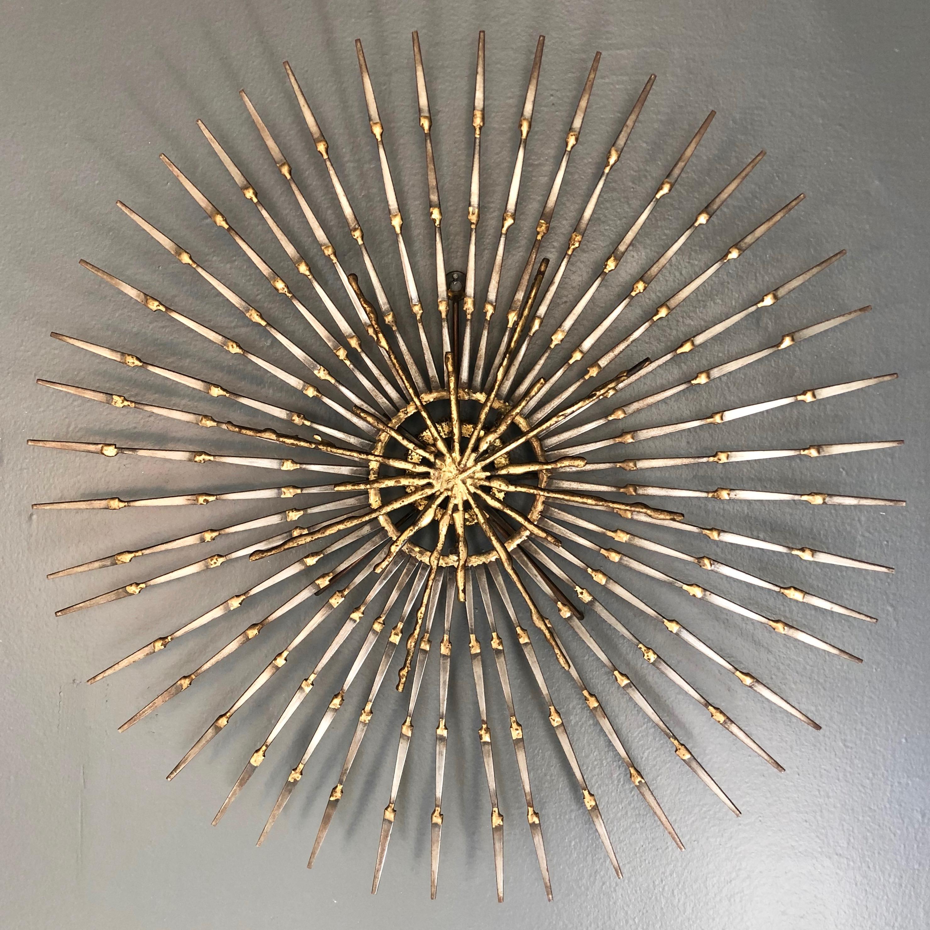 A large Brutalist sunburst with starburst overlay nail art wall sculpture by Ron Schmidt.

Very uncommon multiplanar design with forty-four brass welded iron nail rays radiating sunburst-style from a central brass ring that floats in front of an
