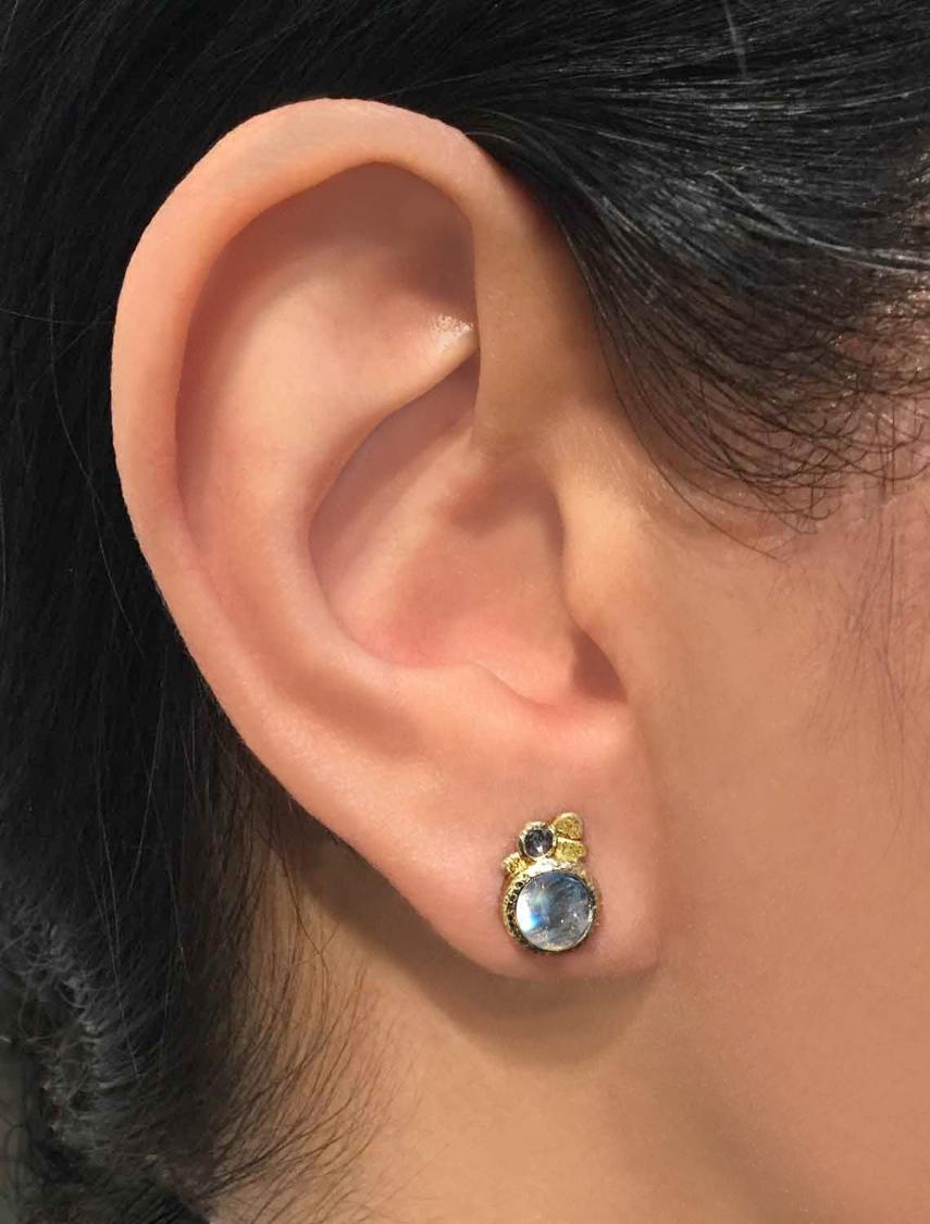 One of a Kind Earrings handcrafted by jewelry maker Rona Fisher featuring a matched pair of glowing blue moonstone, bezel-set in beautifully-textured 18k yellow gold and accented by a pair of round rose-cut salt and pepper diamonds. Stamped and