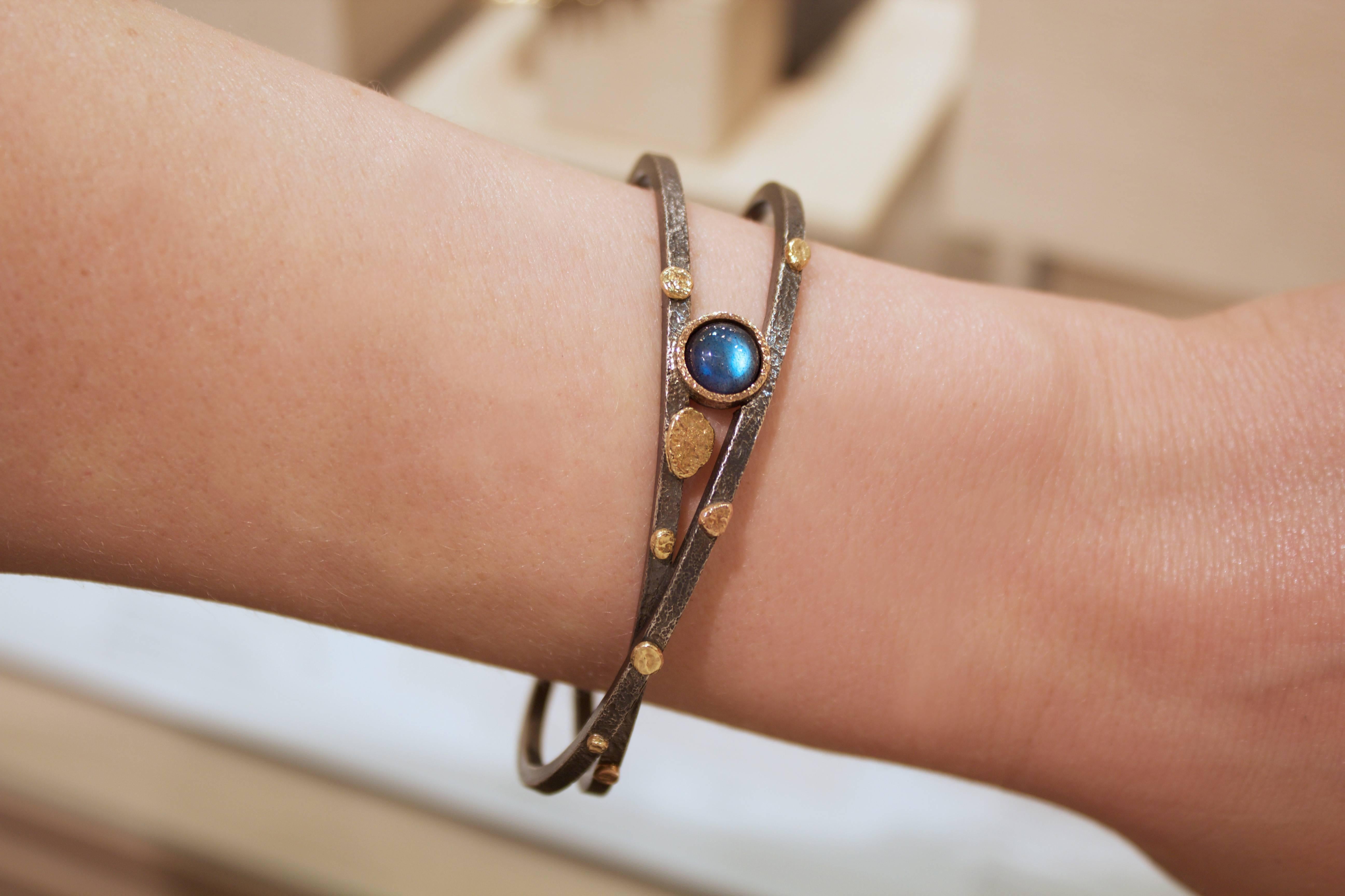 One of a Kind Criss Cross Bracelet handcrafted by jewelry artist Rona Fisher in highly textured oxidized sterling silver featuring a vibrant labradorite cabochon wrapped in 18k rose gold and accented by six 18k yellow gold and two 18k rose gold