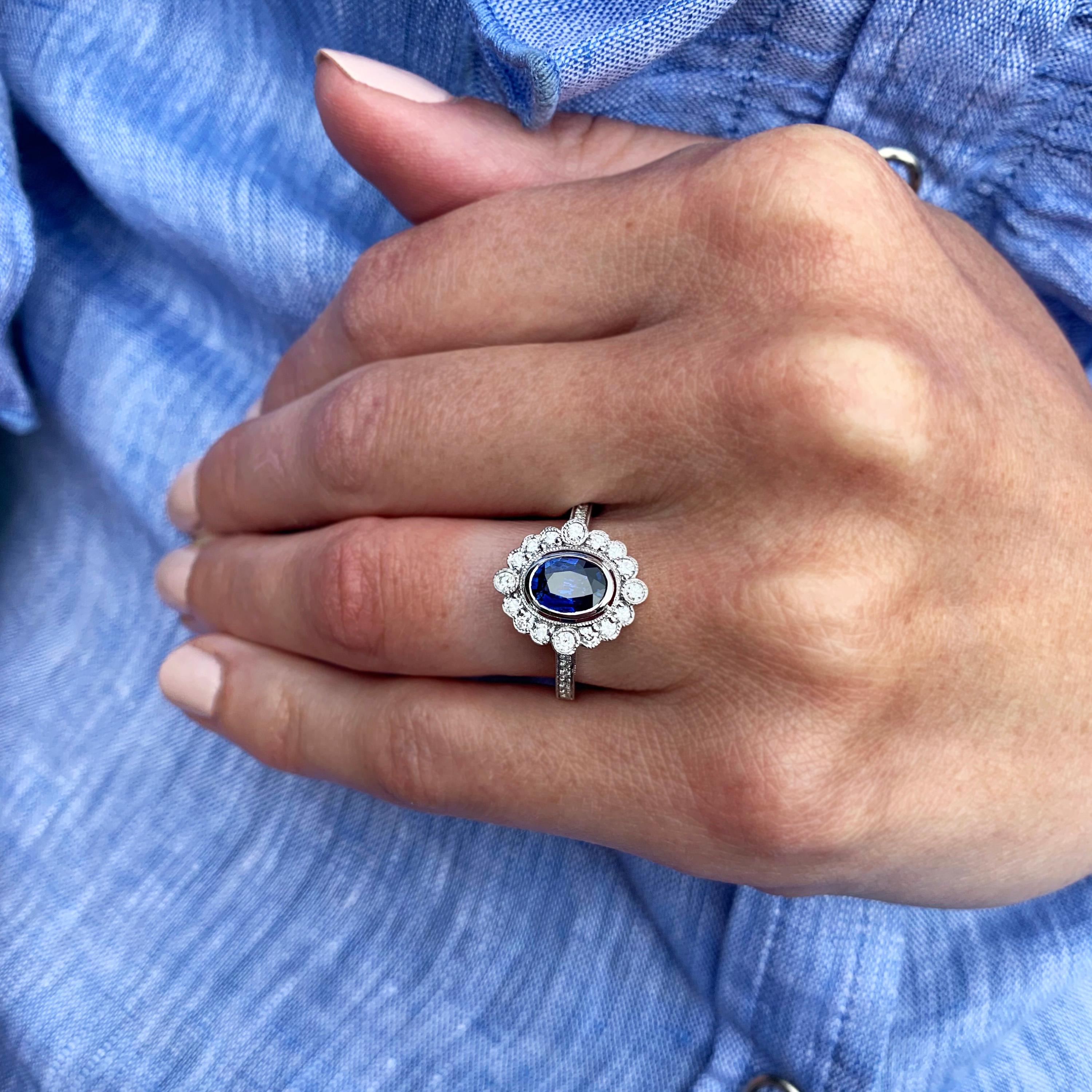 A beautiful sapphire and diamond engagement ring made in 18k white gold. Vintage inspired alternative engagement ring set with gorgeous vibrant blue oval sapphire (0.88ct). A vintage style halo surrounds the neat bezel setting with intricately set