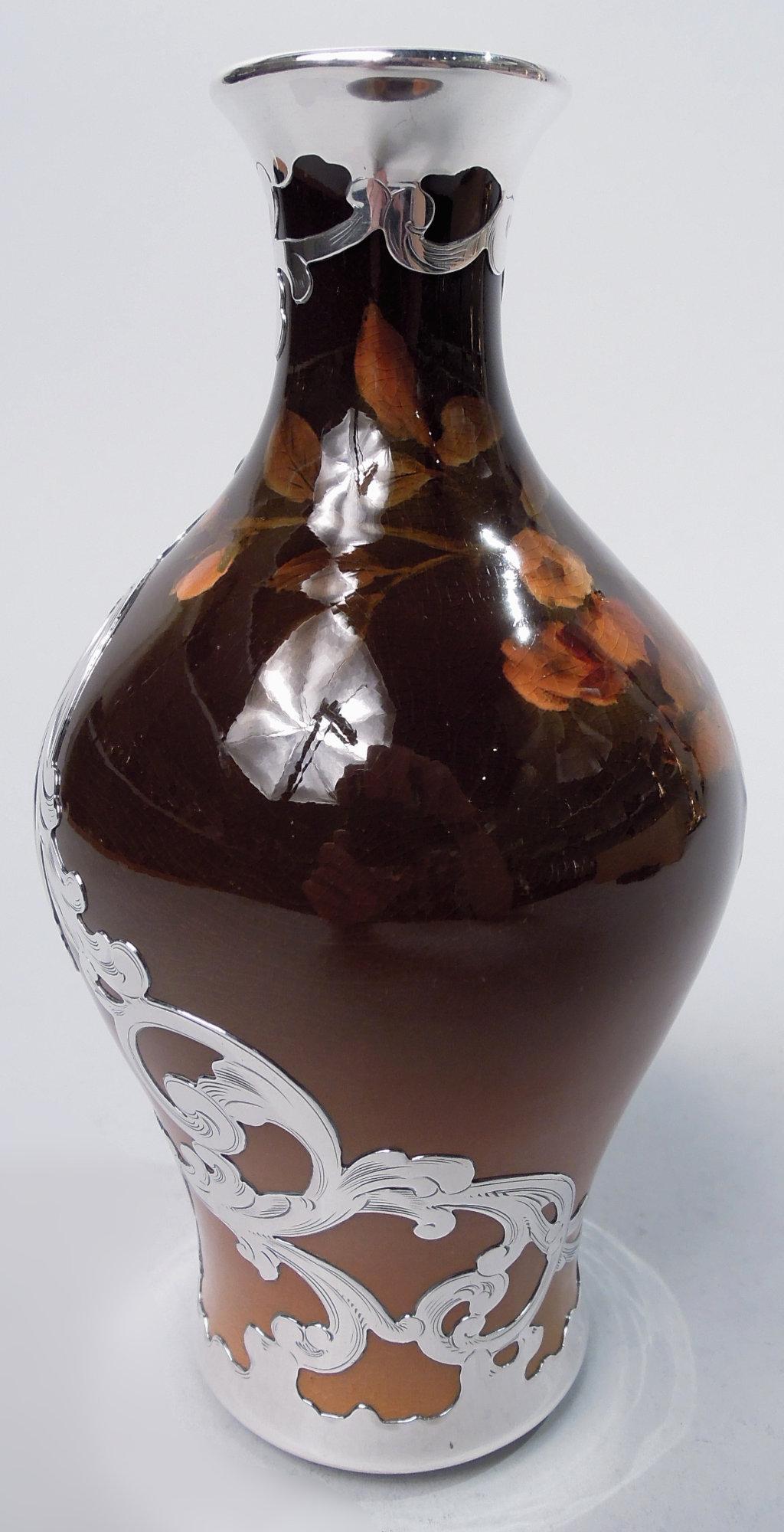 Vase Art Nouveau Craftsman en faïence émaillée avec un revêtement en argent gravé. Fabriqué par Rookwood Pottery à Cincinnati en 1896. Balustre à col cylindrique. Branche fleurie peinte avec de petites fleurs vaporeuses. Sol brun ombragé.