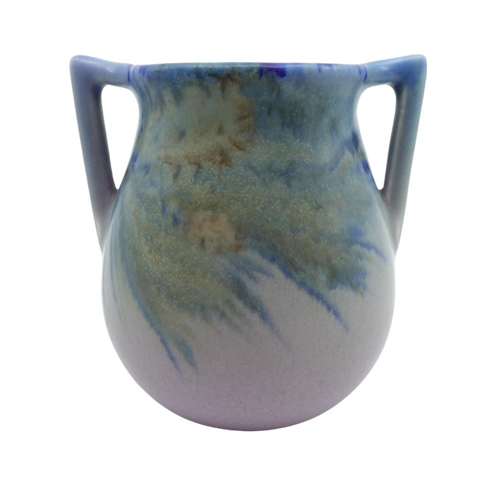 Offering this gorgeous hand-painted Rookwood pottery vase featuring a hand-painted stylized pine cone and branch design. This vase is hand-painted with beautiful hues of blue, mauve, violet and cream. Vase is artist signed 