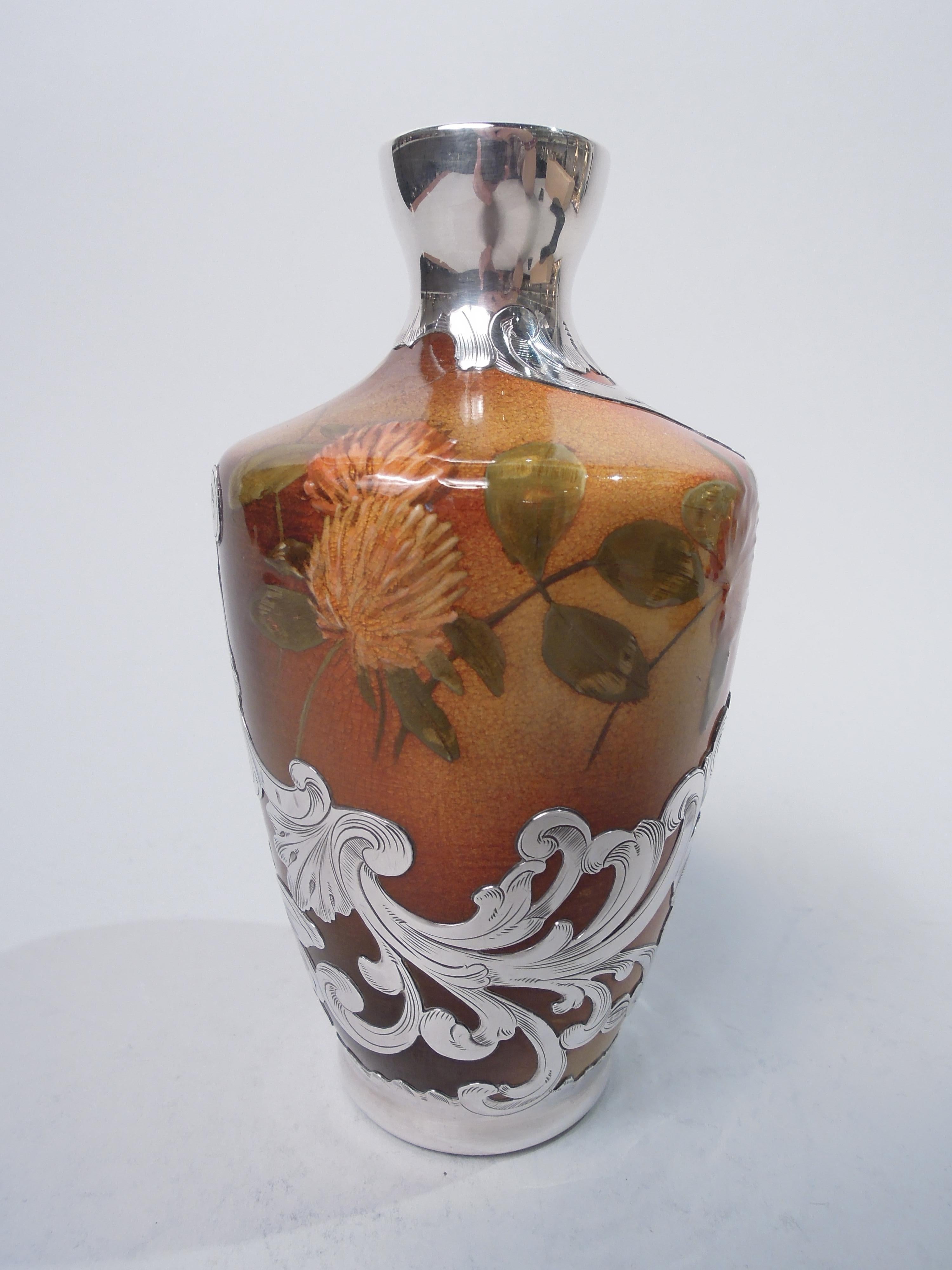 Art Nouveau Craftsman glazed earthenware vase. Made by Rookwood Pottery in Cincinnati in 1892. Tapering sides white shoulder and short neck in silver collar. Painted clover on shaded yellow orange ground. Spare scattered wildflowers contrasting with