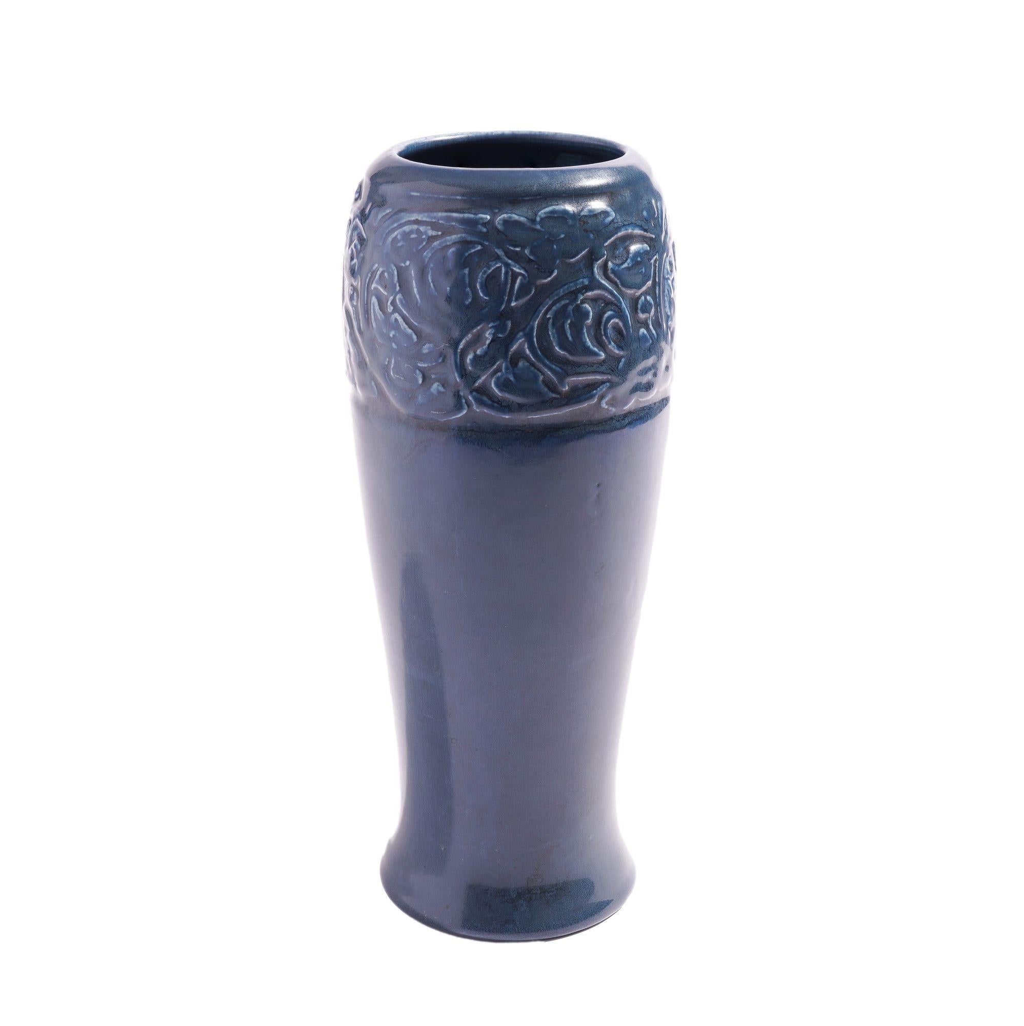 Vase aus blau glasierter Keramik mit breitem, eingeprägtem Blumenband, das die Oberseite umgibt, unter einer umgedrehten Lippe. Die subtile Form der sich leicht verjüngenden Ausbuchtung von der umgedrehten Lippe zu einer taillierten Basis mit