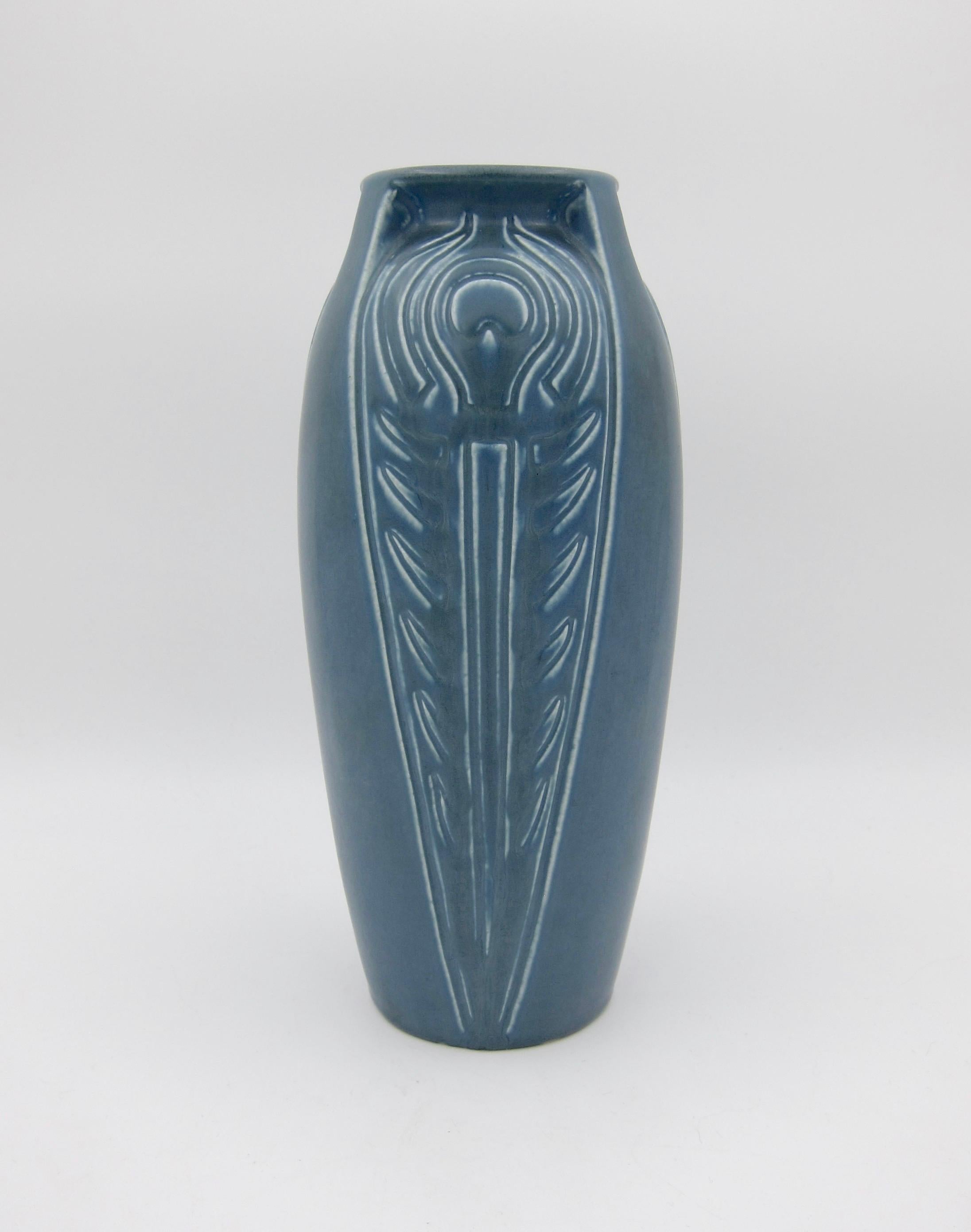 A Rookwood Pottery buttressed vase with a peacock feather motif repeating three times around the vessel. The American art pottery vase is a substantial production piece covered in a velvety blue matte glaze and date marked 1921. Very good condition,