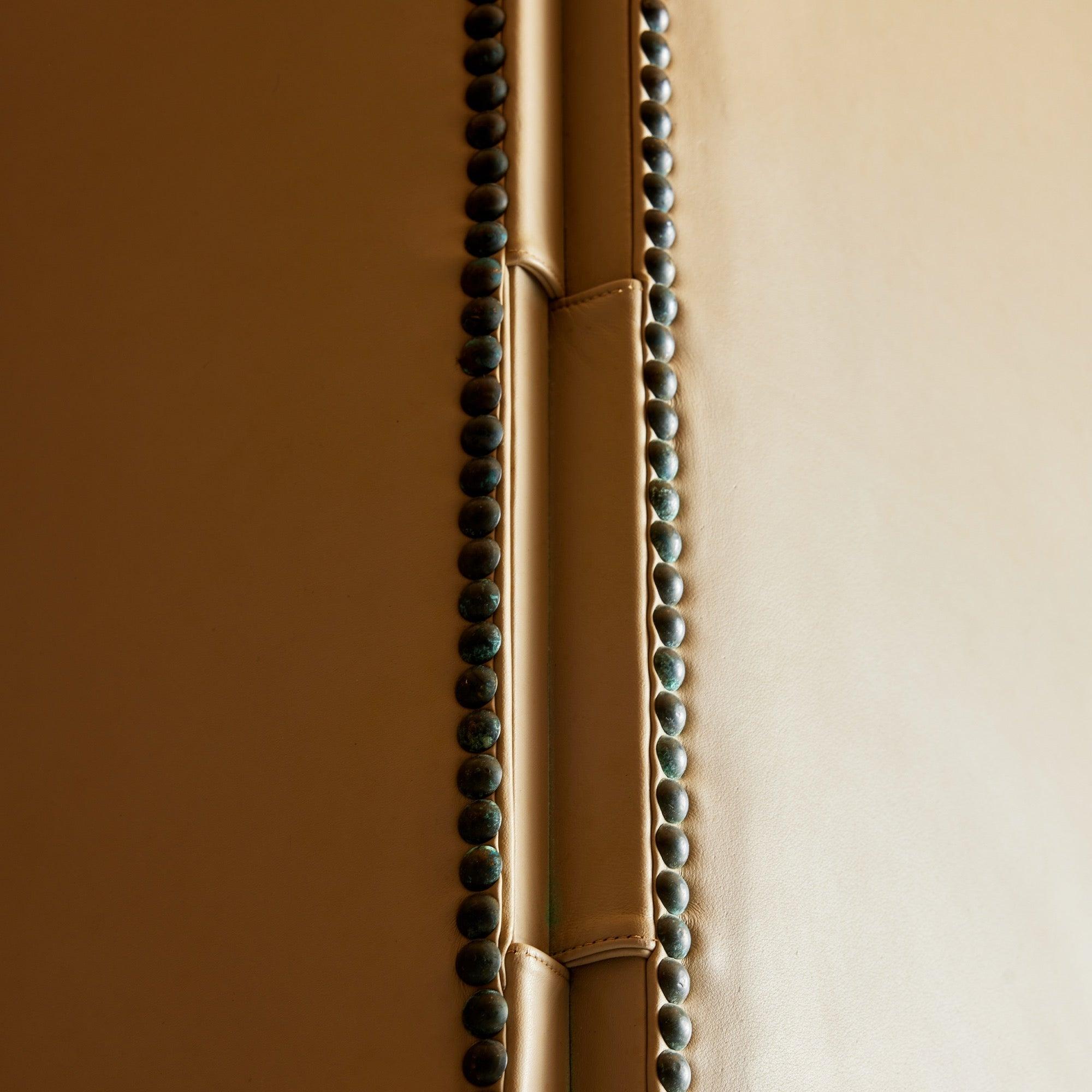 A cream leather room divider consisting of three separate panels each connected using leather hinges and adorned with studded hardware along the edges.