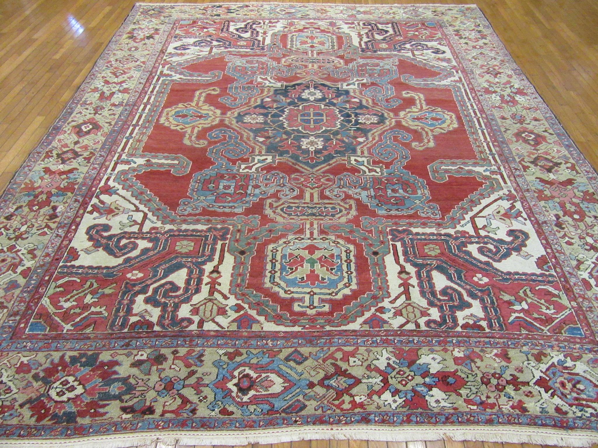 This is a Classic antique hand knotted Persian Heriz rug. It is made with wool pile and cotton foundation. The rug has the trade mark central and corner medallion geometric Heriz pattern in primary colors of red, blue and beige made with natural