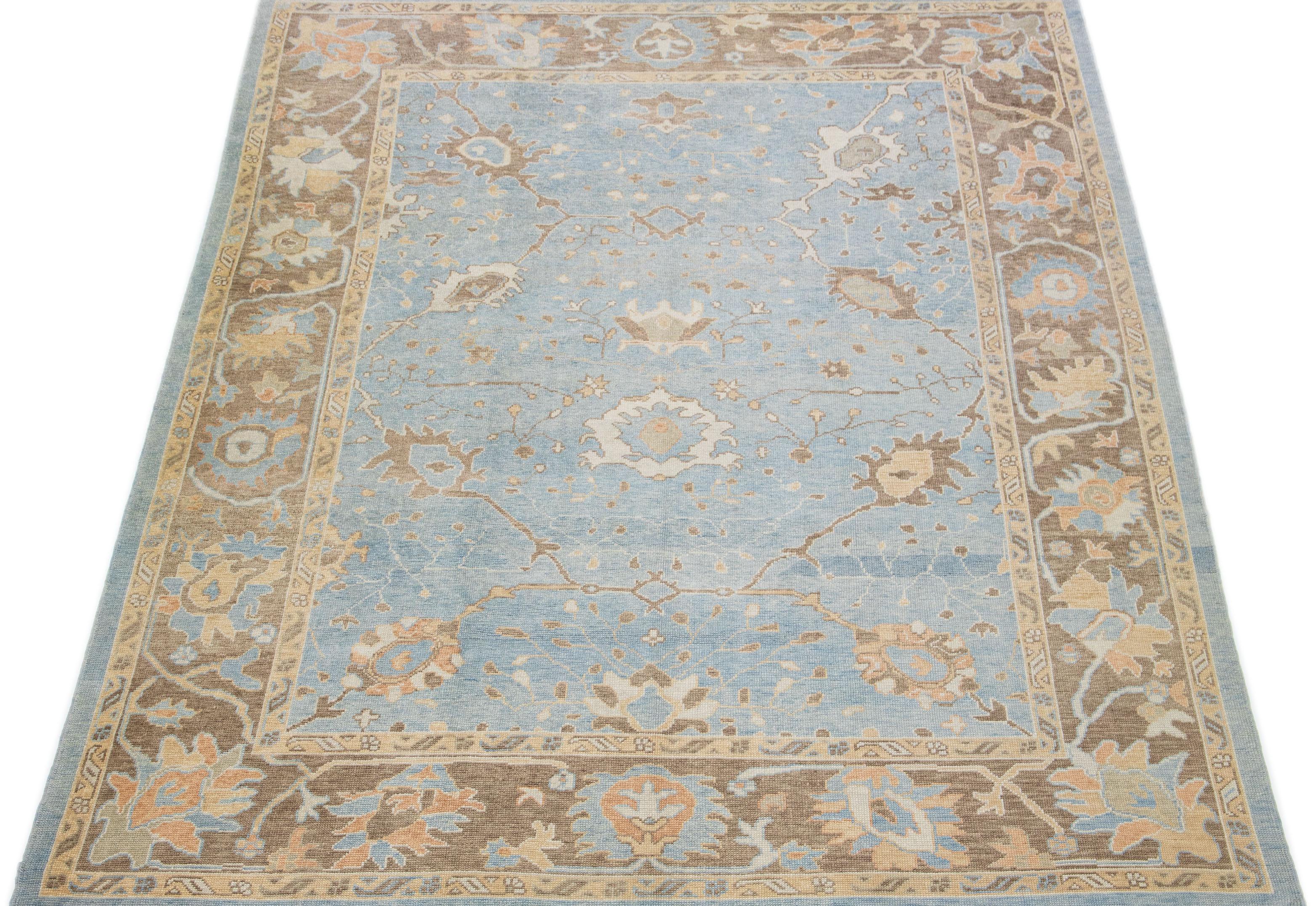 This woolen rug from Oushak, Turkey, boasts a modern aesthetic, featuring a delightful floral pattern in shades of beige on a beautiful blue canvas. Intricately and expertly crafted by hand, the rug is punctuated with charming accents of cream and