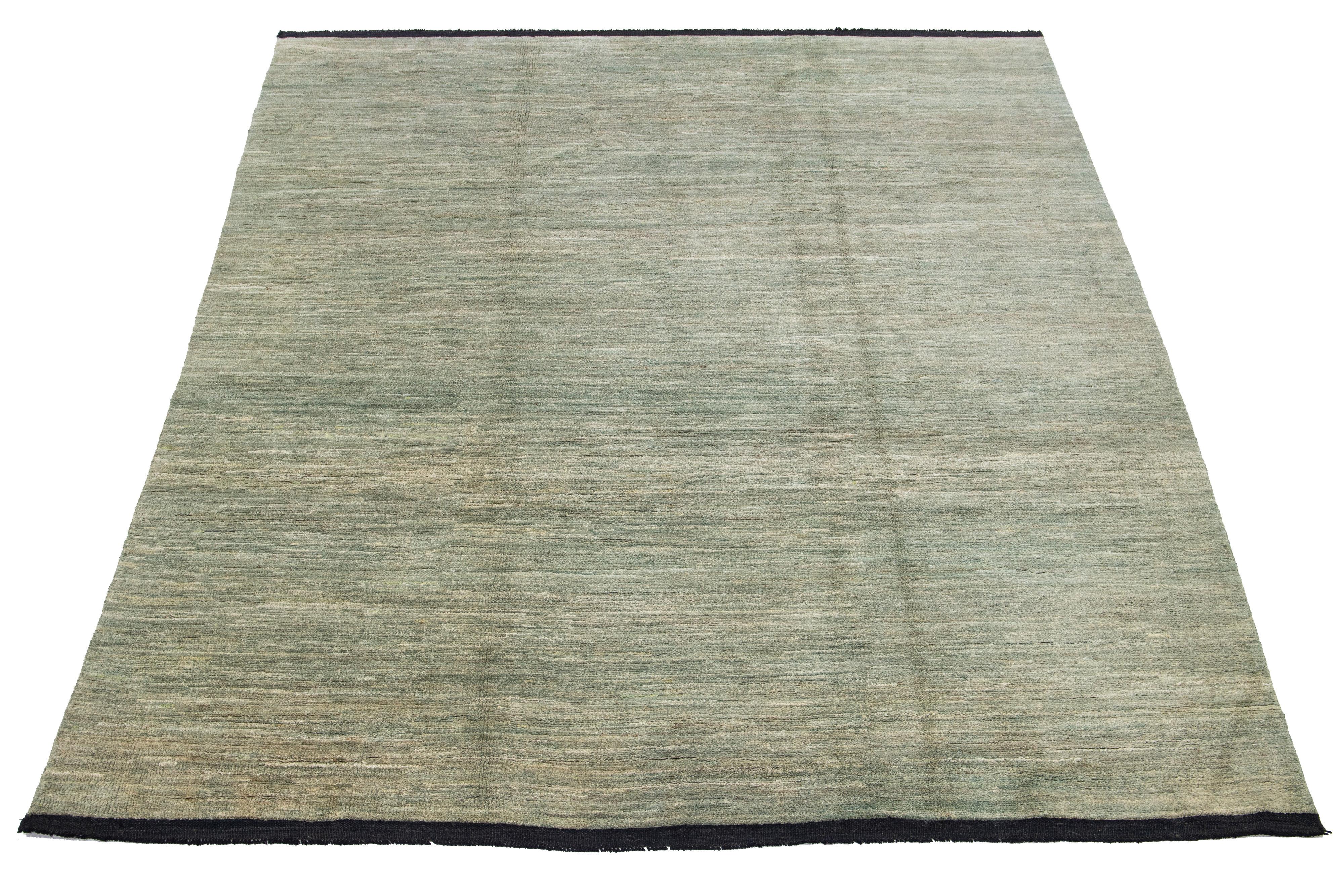 Dieser handgefertigte Wollteppich im Gabbeh-Stil zeigt ein unifarbenes Muster, das durch grüne Schattierungen vor einem leuchtenden beigen Hintergrund akzentuiert wird.

Dieser Teppich misst 7'9