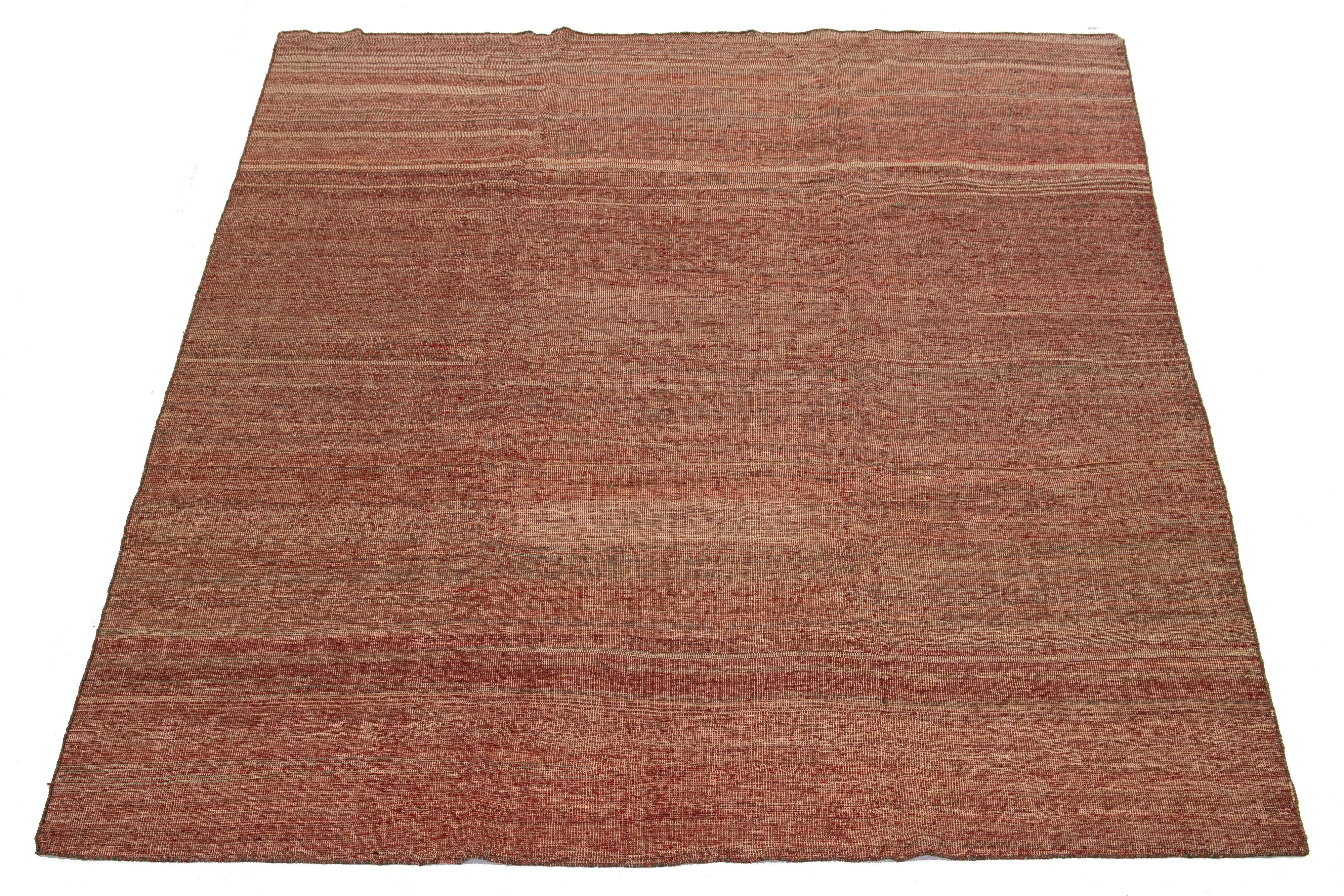 Dieser Teppich zeichnet sich durch ein modernes Kilim-Flachgewebedesign aus Wolle aus, das ein Streifenmuster auf rotem, beigem und grünem Grund zeigt. 

Dieser Teppich misst 8'9