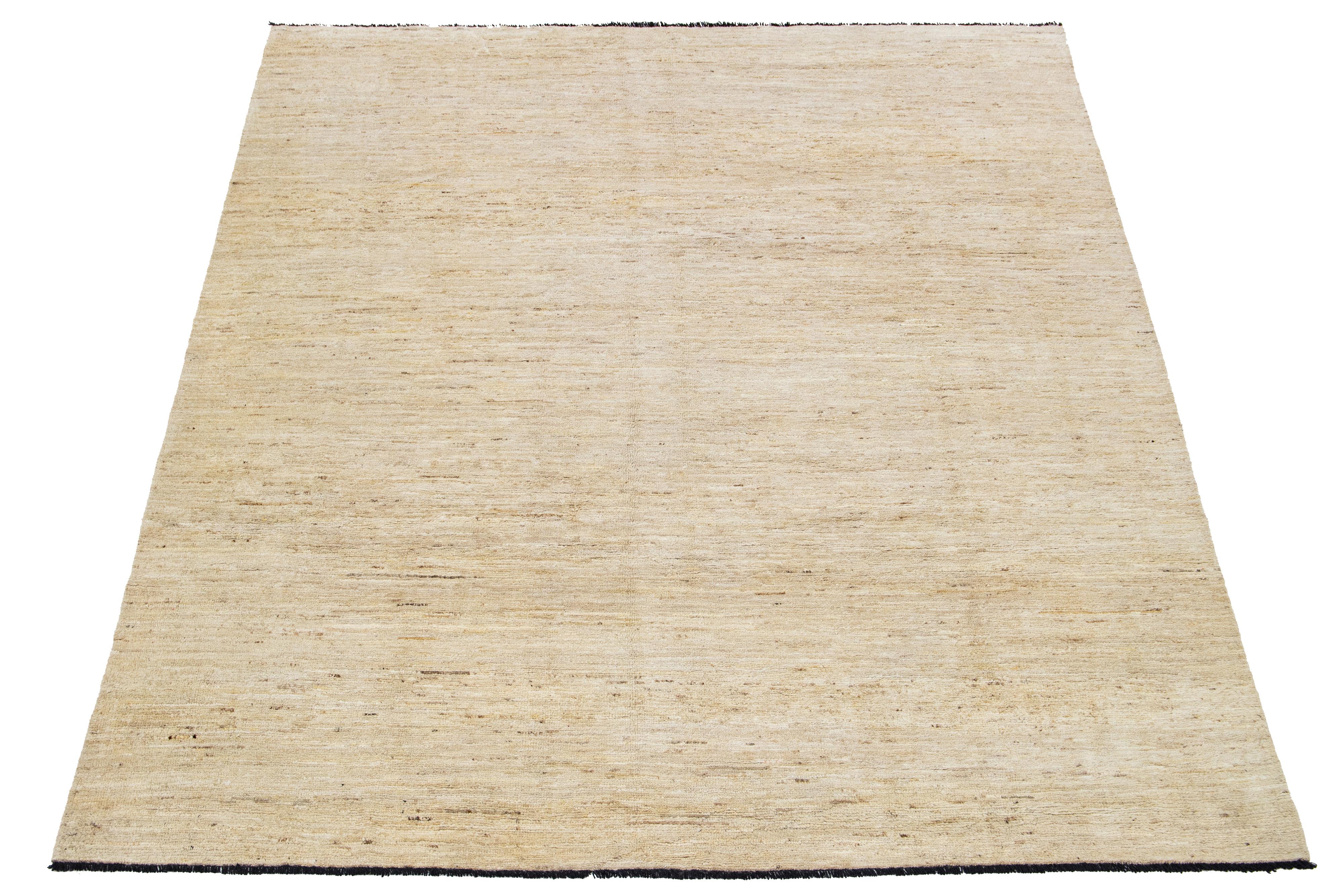 This handcrafted wool rug, designed in the Gabbeh style, showcases a solid design accentuated by brown shades against a beige background with black fringes.

This rug measures 8'2