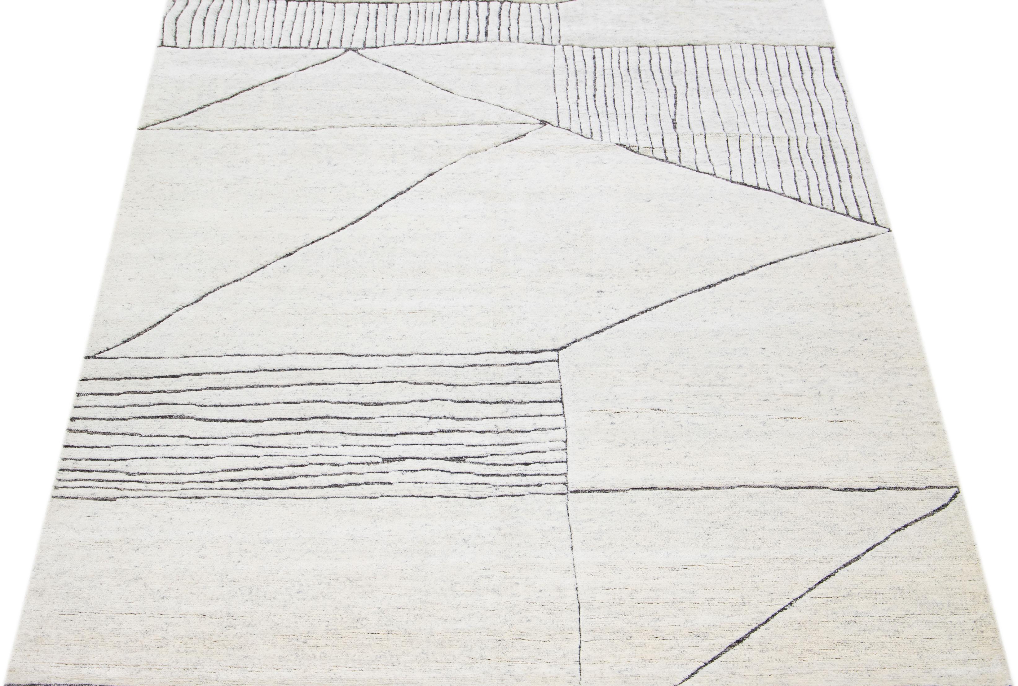 This luxurious wool rug features a timeless Moroccan pattern in a contemporary abstract Minimalist style, utilizing ivory and gray tones to create a sleek and modern look. It is crafted using traditional hand-knotting techniques, ensuring